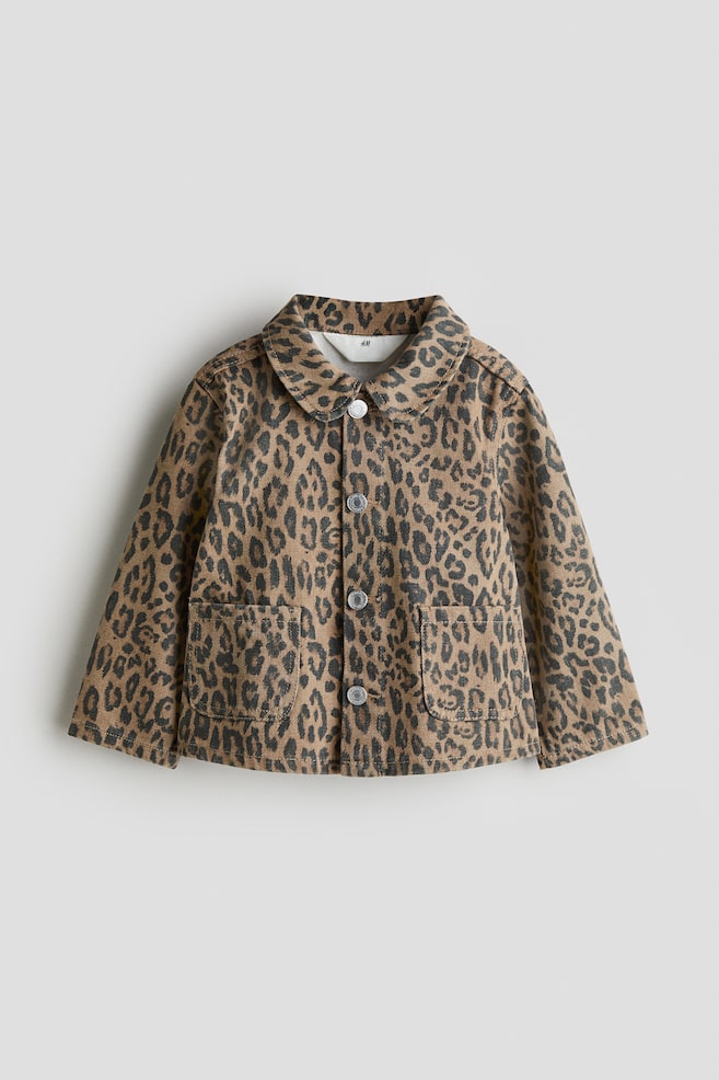 A front view of a tan and dark gray leopard print denim jacket is being shown. It is featuring a rounded collar, a front button closure with four silver-toned buttons, and two large patch pockets on the lower front. - 1