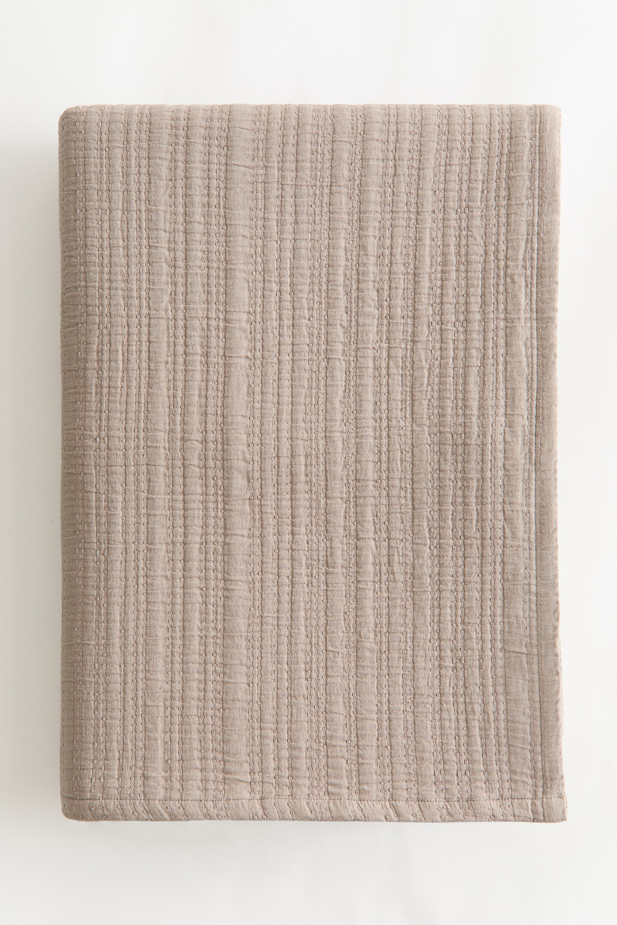 View larger image: A single bedspread crafted from soft cotton muslin weave showcases its front surface. It features a light brown hue with a textured pattern of narrow vertical raised stripes.