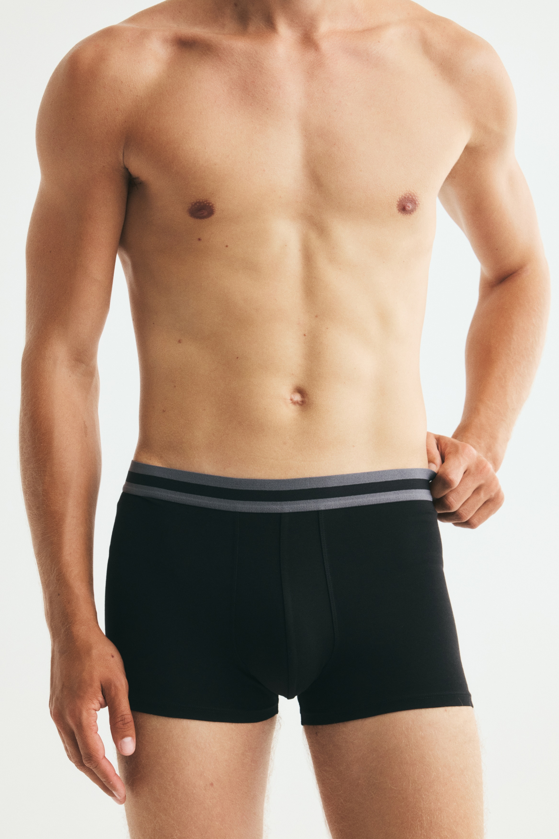 Drei schwarze Boxershorts liegen gestapelt, nach vorne gerichtet. Jede Shorts verfügt über einen elastischen Bund mit zwei horizontalen schwarzen Streifen. Der obere Bund ist burgunderrot, der mittlere grau und der untere hellblau.