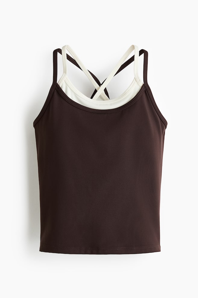 A dark brown camisole top featuring a scoop neckline and thin spaghetti straps, revealing an off-white inner layer with wider straps that cross at the back. - 1