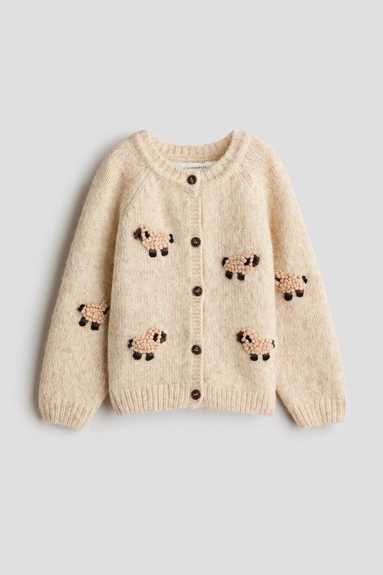 Un cardigan en tricot de couleur crÃ¨me est prÃ©sentÃ© de face, avec un col rond cÃ´telÃ©, des poignets et un ourlet cÃ´telÃ©s, ainsi quâune fermeture boutonnÃ©e Ã  lâavant avec cinq boutons brun foncÃ©. Le cardigan arbore plusieurs petits motifs de moutons texturÃ©s, avec des corps de style bouclÃ© et des dÃ©tails brodÃ©s brun foncÃ©, rÃ©partis sur le devant et les manches.