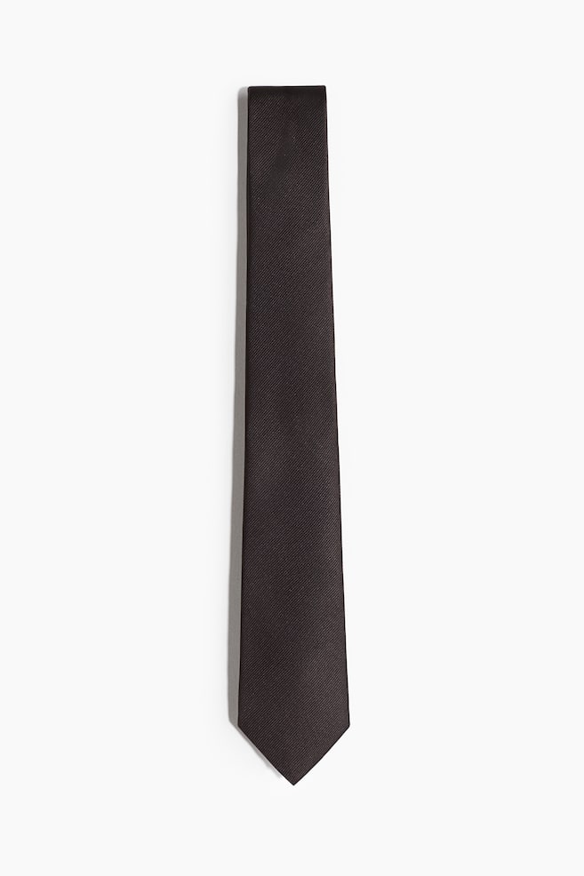 A dark woven tie is lying flat, facing front. It is featuring a subtle diagonal twill texture and is measuring 7 cm in width at its widest point. - 1