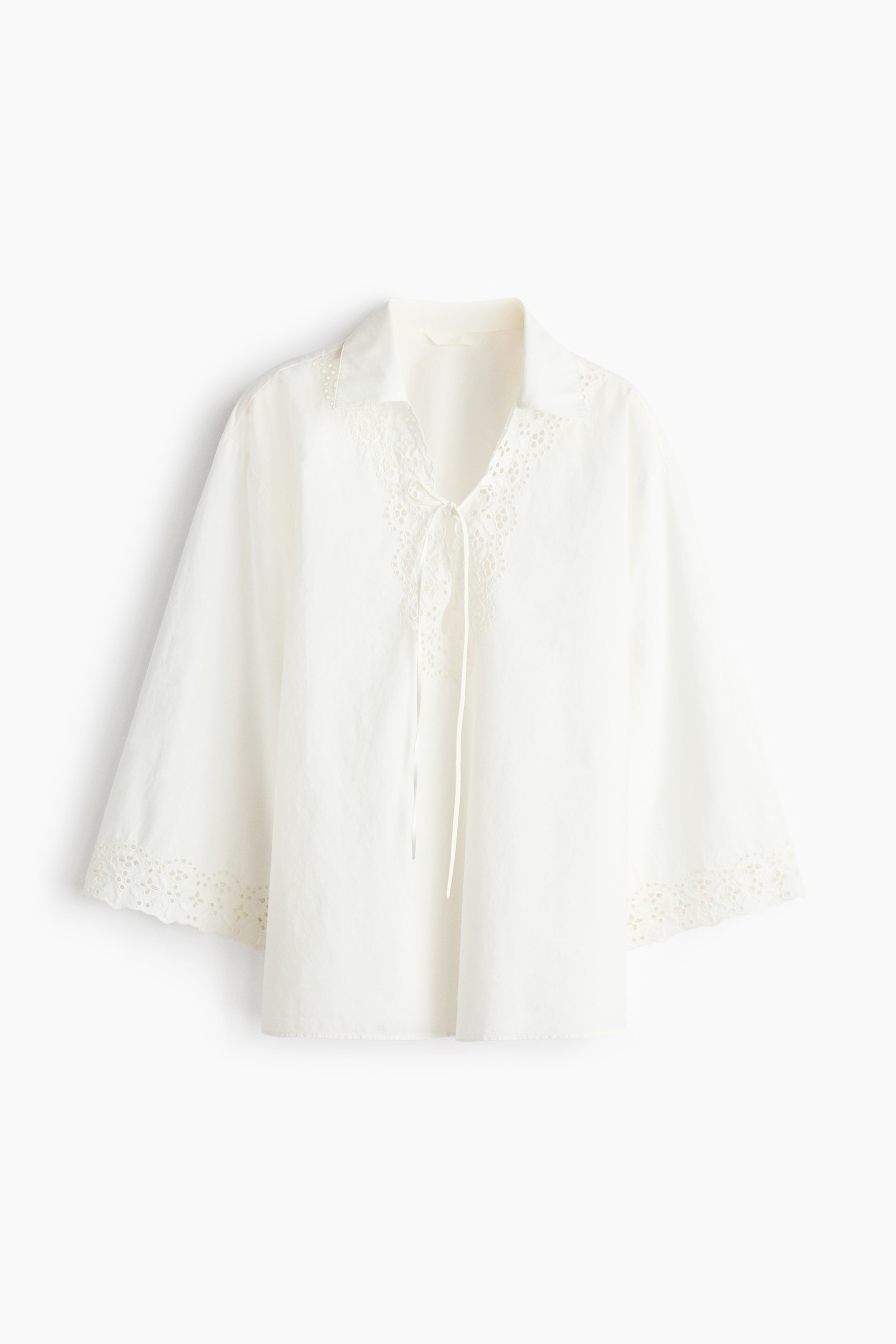 View larger image: The white top features a spread collar and a V-neckline with a tie detail. It showcases broderie anglaise trim around the neckline and the hems of its three-quarter length sleeves, presenting a relaxed fit from the front.