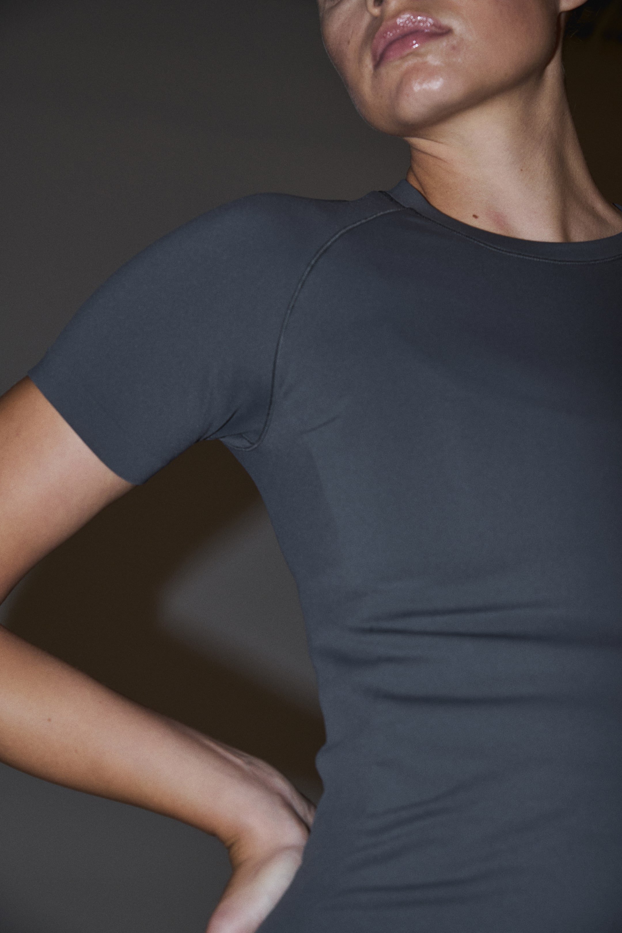Ampliar la imagen: Se lleva puesta una camiseta de manga corta color gris oscuro, con una silueta ajustada, cuello redondo y mangas raglán realzadas por costuras oscuras.