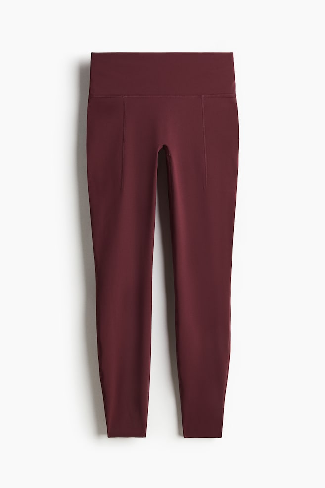 Burgundy leggings are presenting a front view, featuring a wide, high-rise waistband and subtle, flat slip pockets on the outer thighs. They are designed with a smooth, fitted silhouette that extends to the ankle. - 1