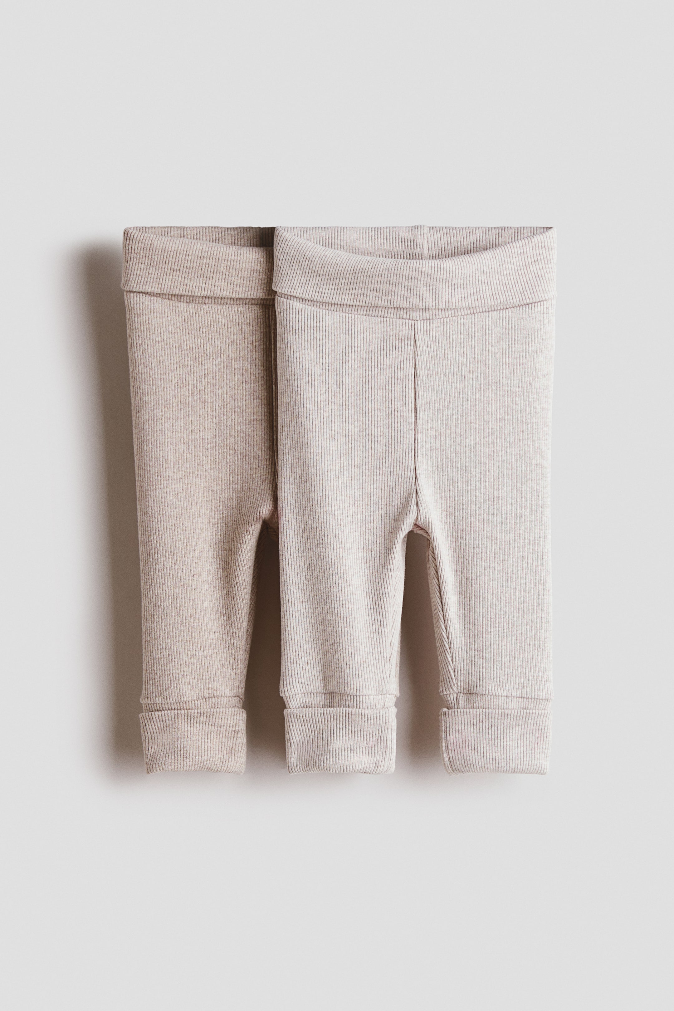 Grotere afbeelding bekijken: Twee paar H&M Adorables baby leggings liggen plat, gezien vanaf de voorkant, met een geribbelde jersey textuur in licht beige en een iets donkerder beige, elk met een brede, omvouwbare band bij de taille en extra lange geribbelde boorden bij de zoom die momenteel omgeslagen zijn.