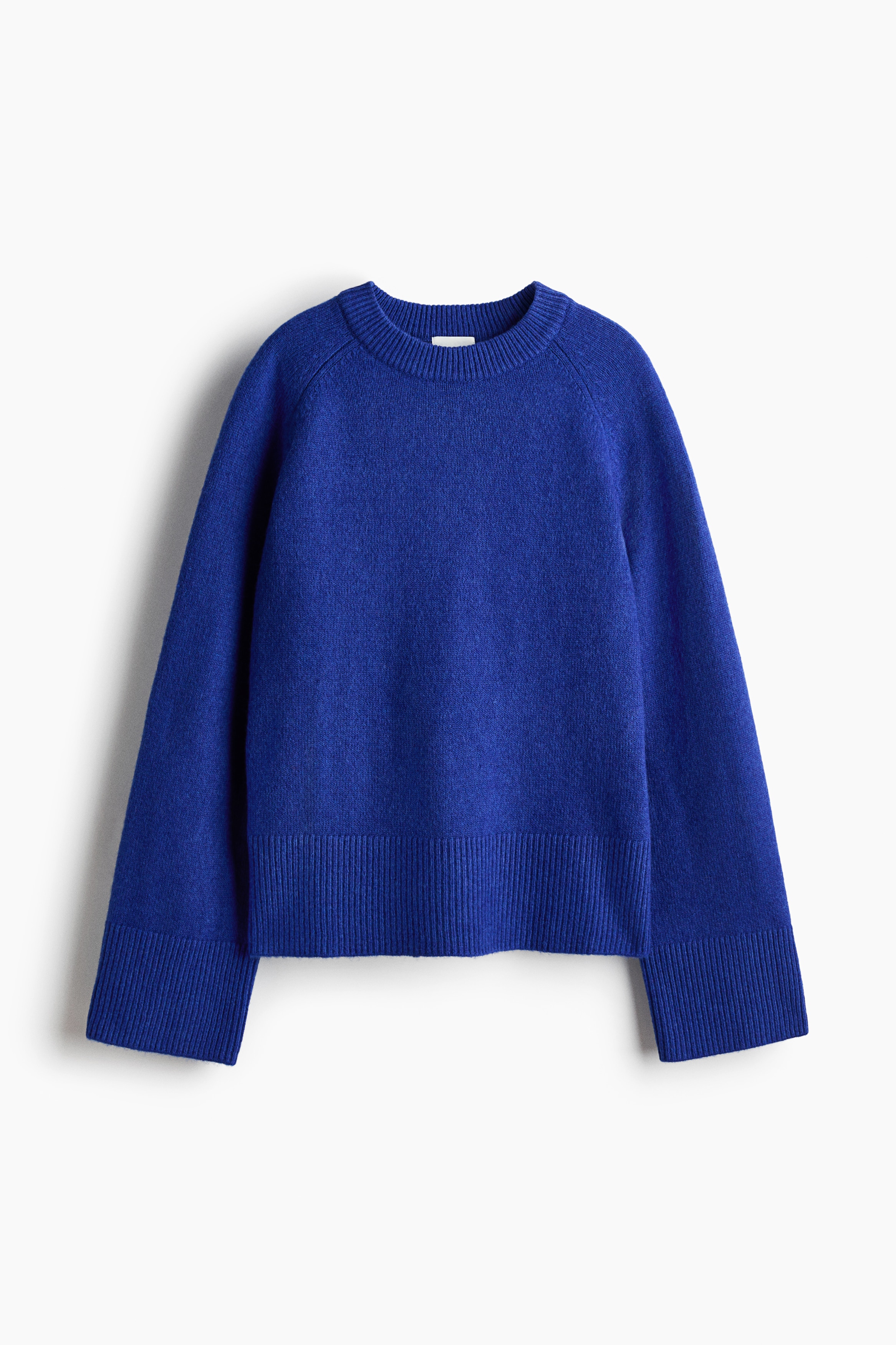 A royal blue knit jumper featuring a round ribbed neckline, long raglan sleeves and a ribbed hem is being worn by the model, who has both arms raised above their head. The jumper is paired with light blue gingham shorts.