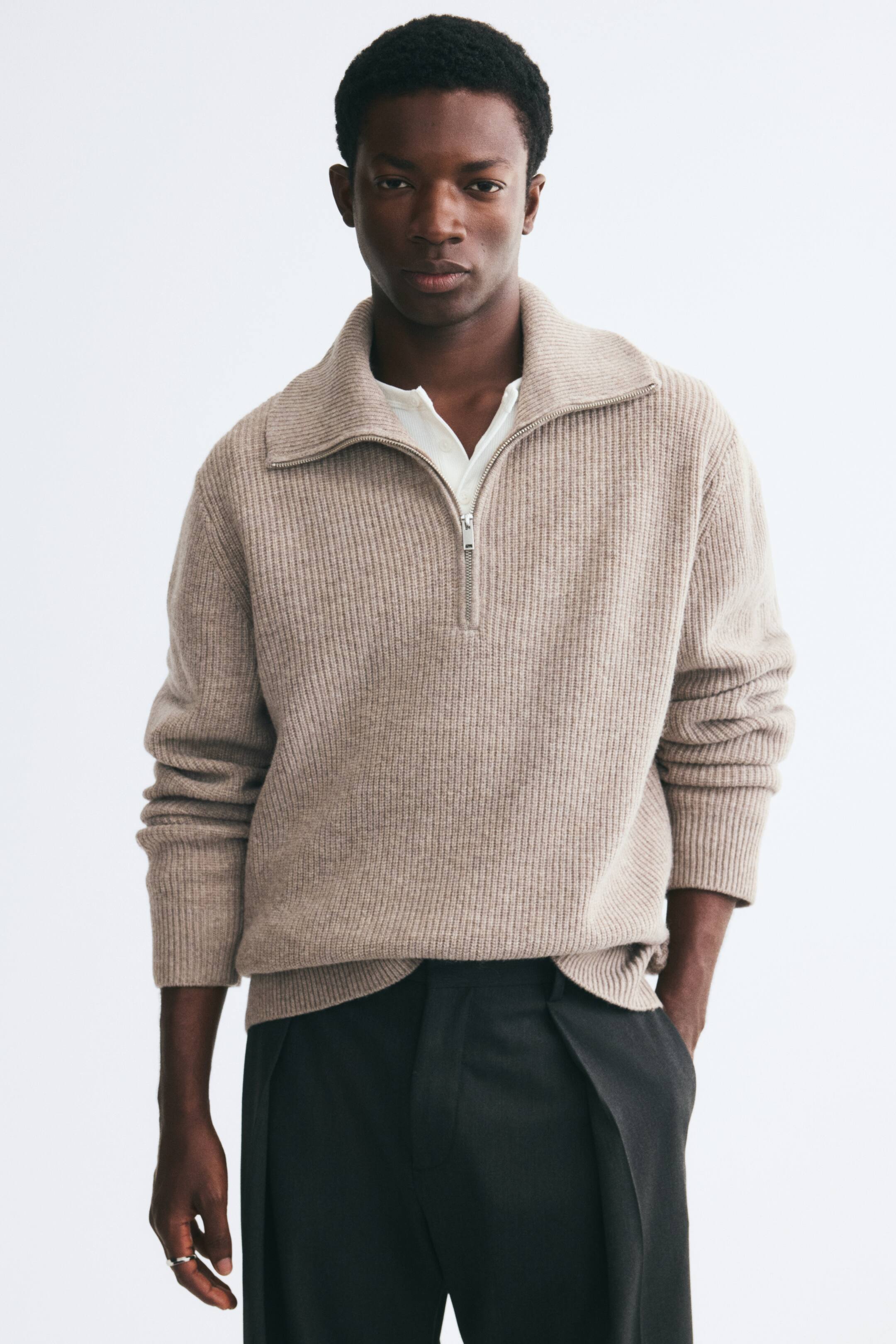 Voir une image plus grande: Un chandail en laine tricotée côtelée beige est porté par le mannequin, superposé à une chemise blanche et à un pantalon foncé. Le chandail présente un col à demi-zip porté ouvert, des manches longues avec poignets côtelés et un ourlet côtelé.