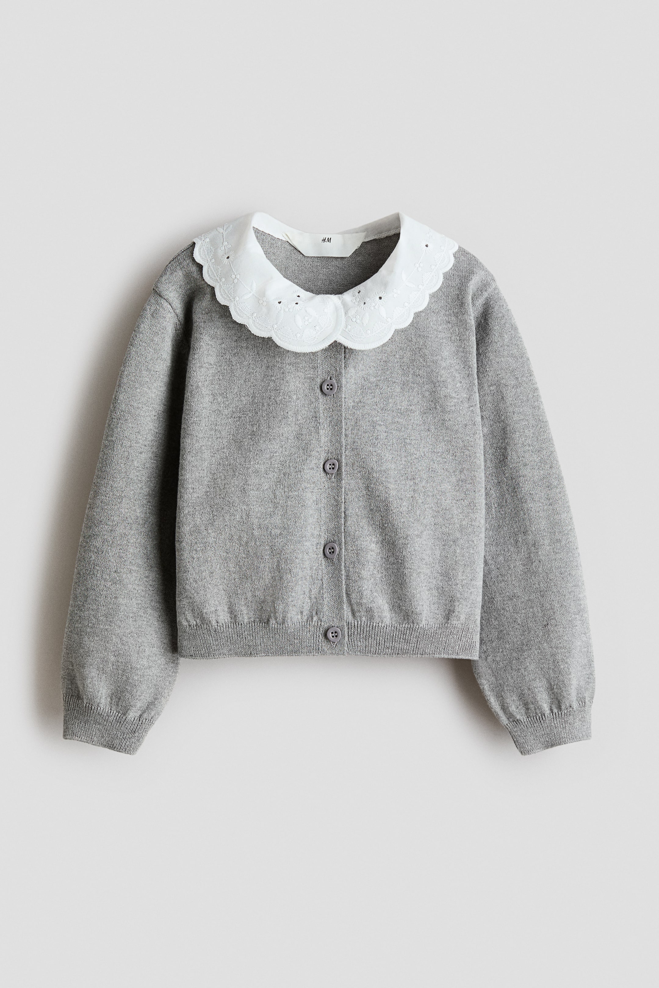 Größeres Bild anzeigen: Ein hellgrauer Feinstrick-Cardigan wird frontal präsentiert. Er verfügt über einen runden Halsausschnitt, einen abgerundeten, gewellten weißen Kragen aus gewebtem Stoff mit Broderie Anglaise, Knöpfe zum Verschließen an der Vorderseite sowie Rippdetails an den Bündchen und am Saum.