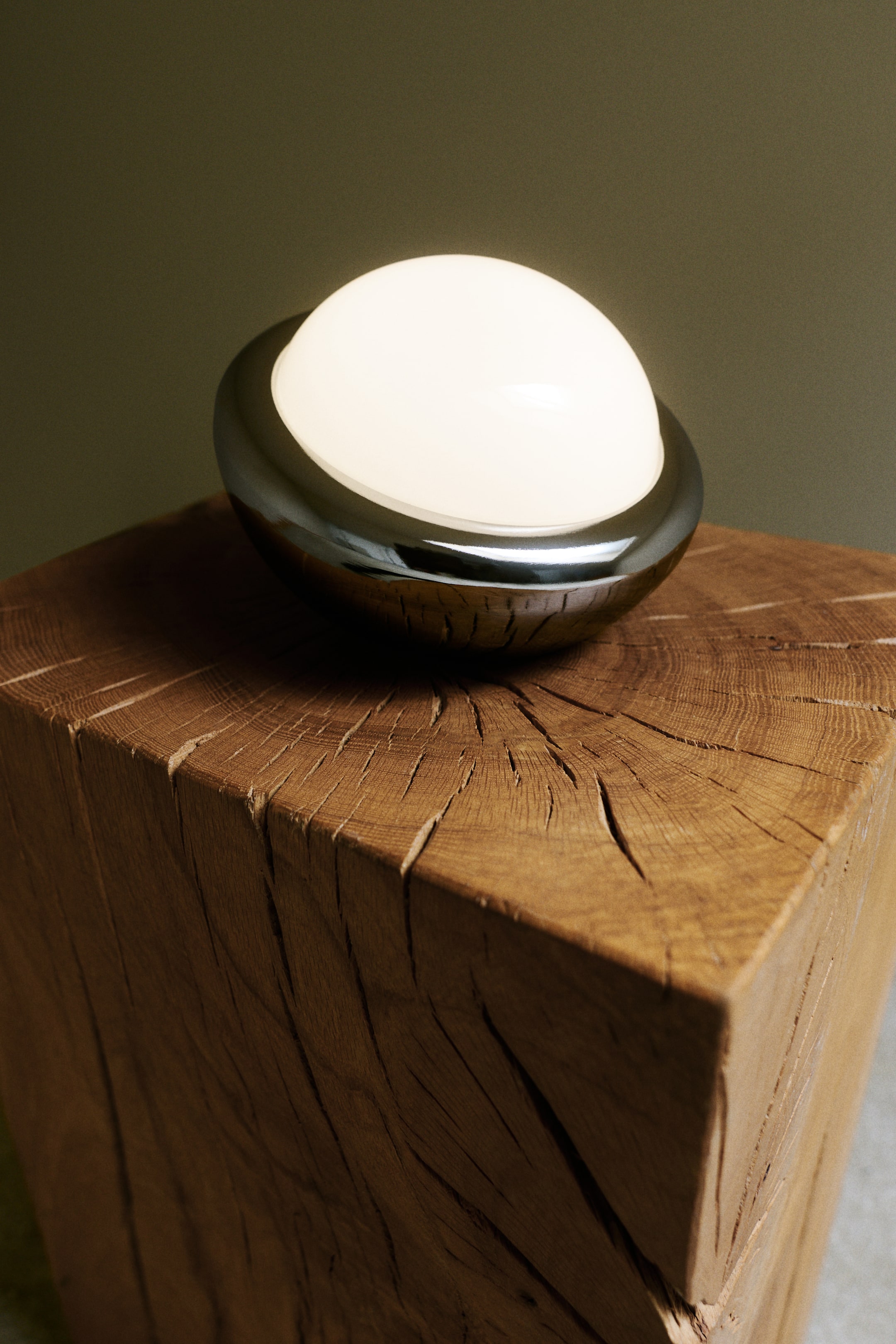 View larger image: A rechargeable table lamp showcasing a gently rounded design, featuring a dark, reflective metal base and an illuminated, semi-spherical opaque white glass top.