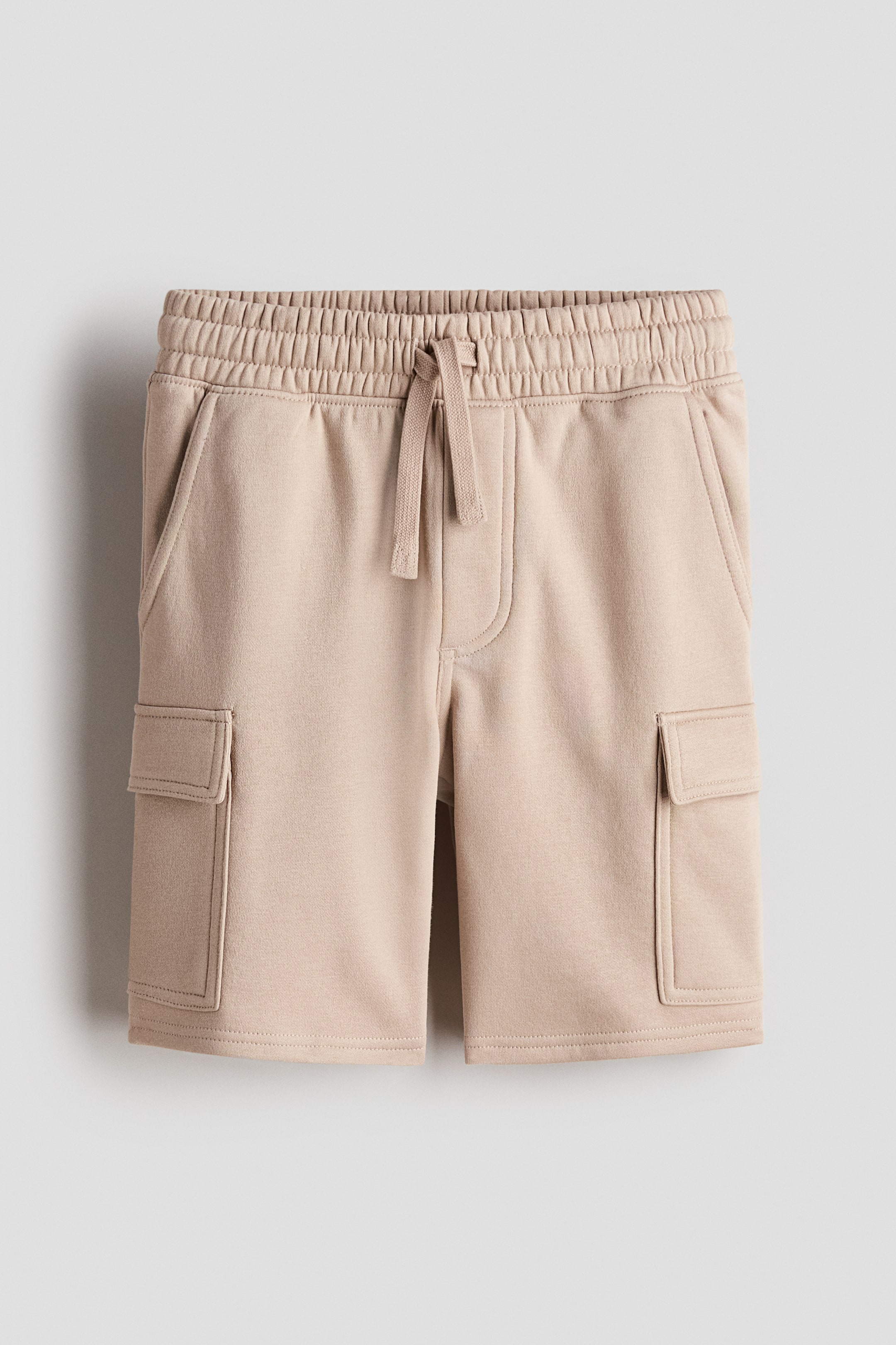 Vezi imaginea mai mare: Pantaloni scurți cargo până la genunchi, din material tip sweatshirt, bej deschis, prezentați din față, având talie elastică cu șnur asortat, braguță falsă, buzunare laterale oblice și buzunare dreptunghiulare cu clapetă pe picior.