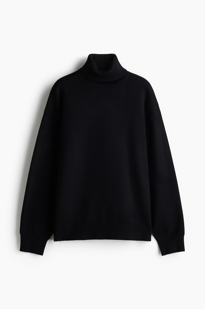 Un pull en maille noir oversize est prÃ©sentÃ© de face, mettant en valeur un col roulÃ© cÃ´telÃ©, des Ã©paules tombantes et des manches longues. Il prÃ©sente des dÃ©tails en fine maille cÃ´telÃ©e au niveau des poignets et de lâourlet, soulignant sa structure dÃ©contractÃ©e et confortable. - 1