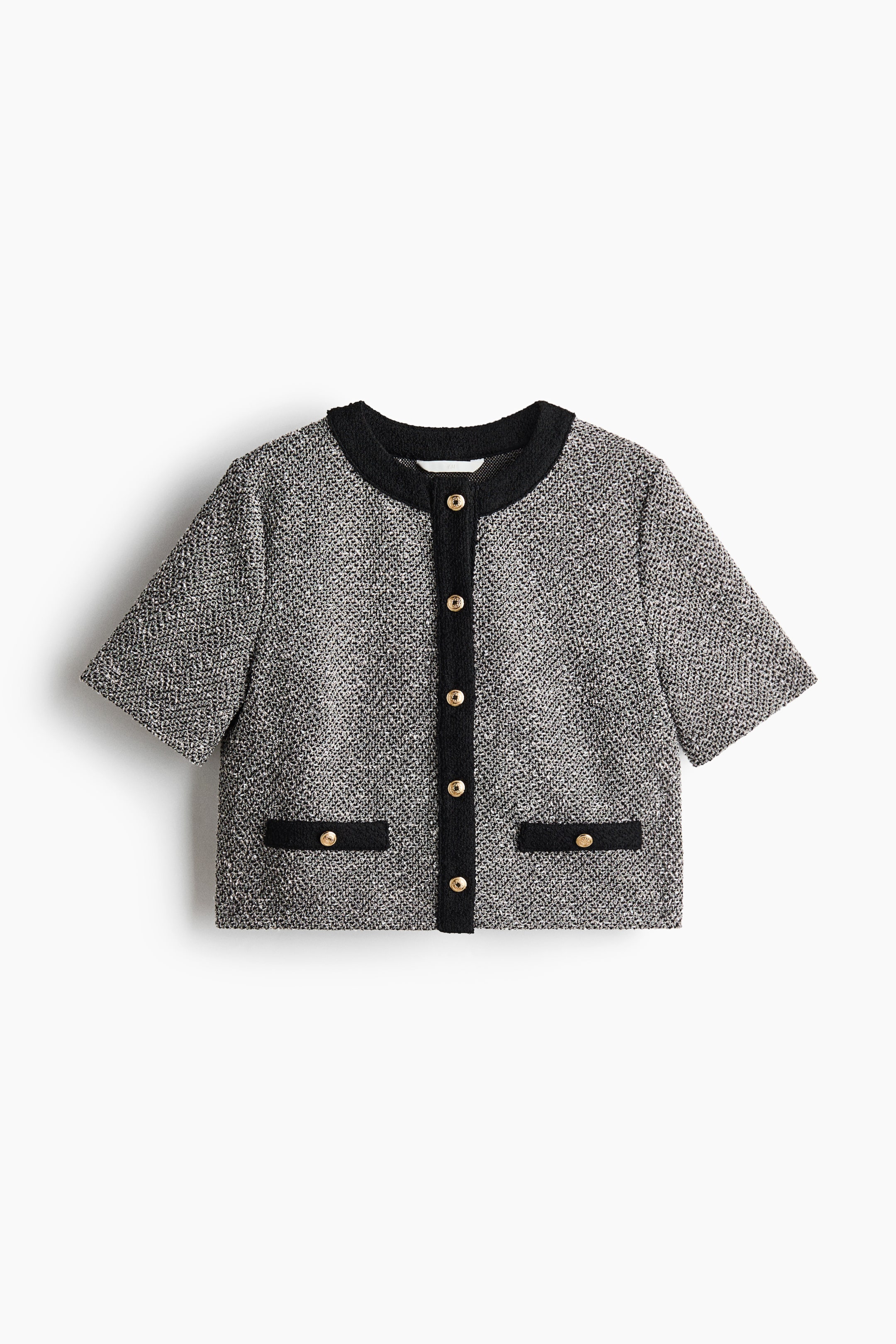 View larger image: A cropped short-sleeve jacket showcases a gray-and-white tweed-like texture. It features black trim along the round collarless neckline, front button placket, and two front pocket flaps, each accented with a gold-toned button.