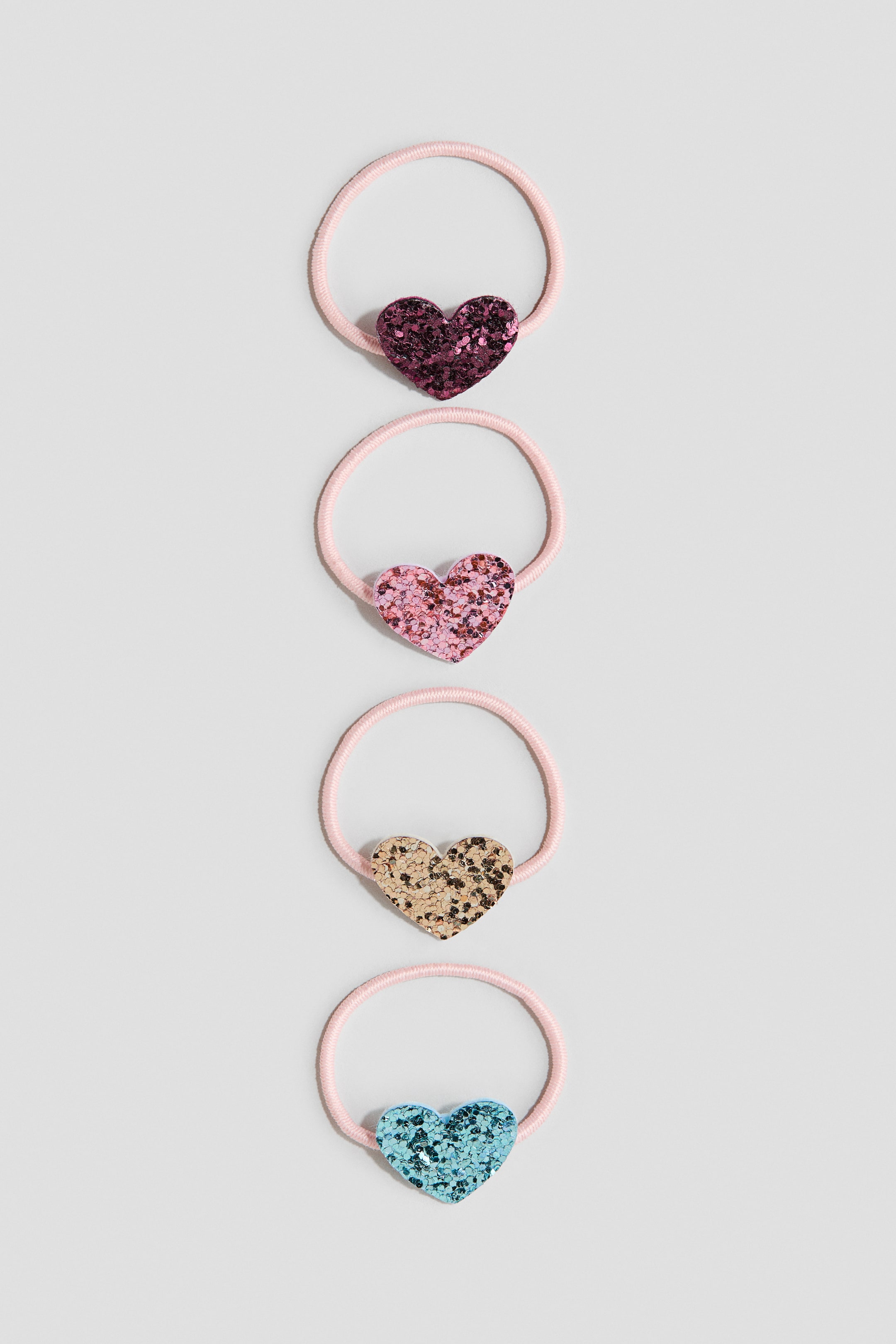 Voir une image plus grande: Quatre élastiques à cheveux sont présentés, empilés verticalement, chacun doté d'une bande élastique rose et d'un charme en forme de cœur recouvert de paillettes à l'avant. Les charmes en forme de cœur apparaissent en violet foncé, rose clair, or et bleu clair.