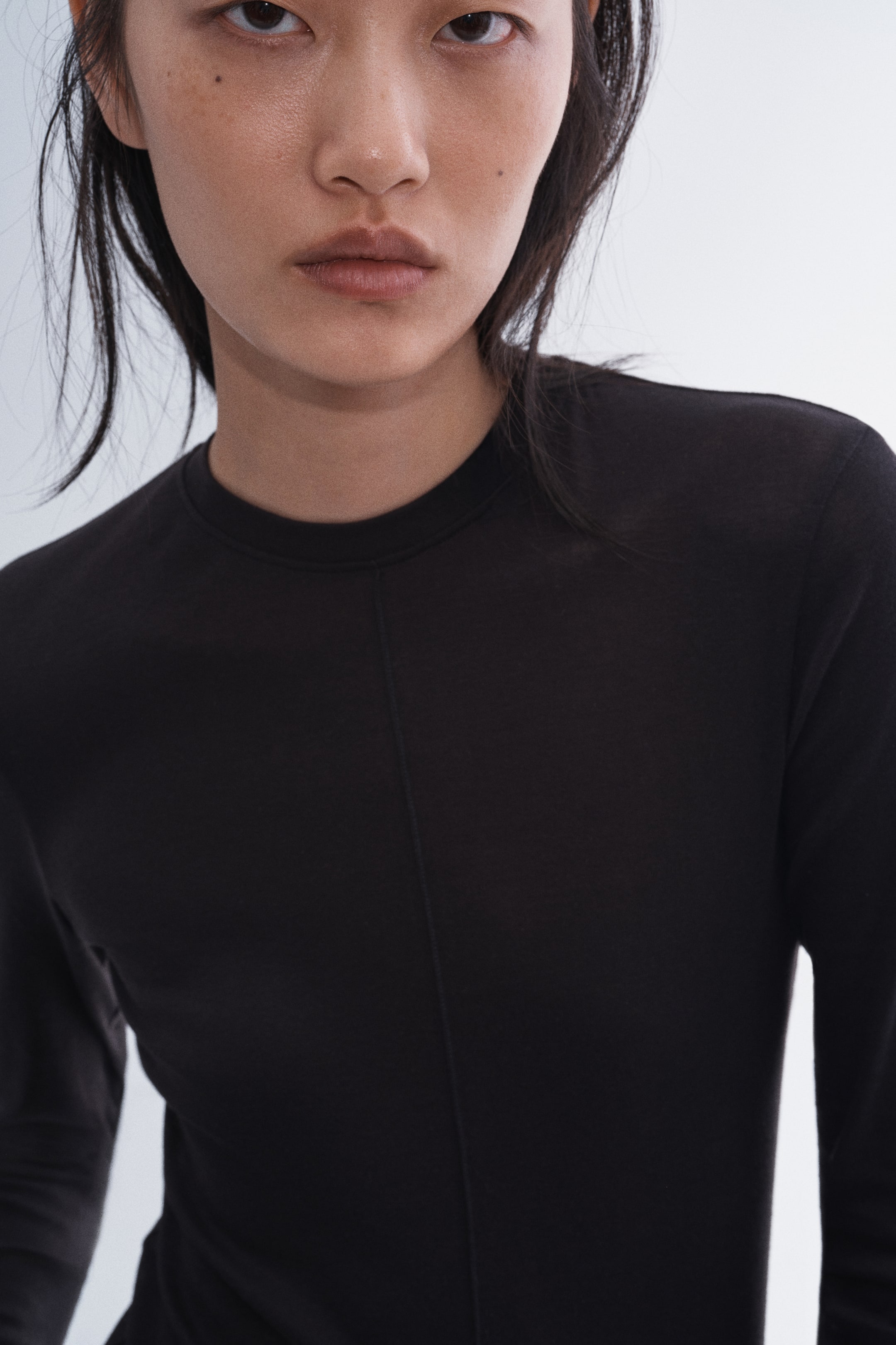 View larger image: The model is wearing a black long-sleeved top. It features a crew neck and a centre seam down the front.
