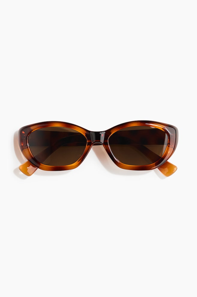 Les lunettes de soleil écaille de tortue présentent des verres ovales et foncés, avec des branches légèrement inclinées vers l'extérieur. - 1