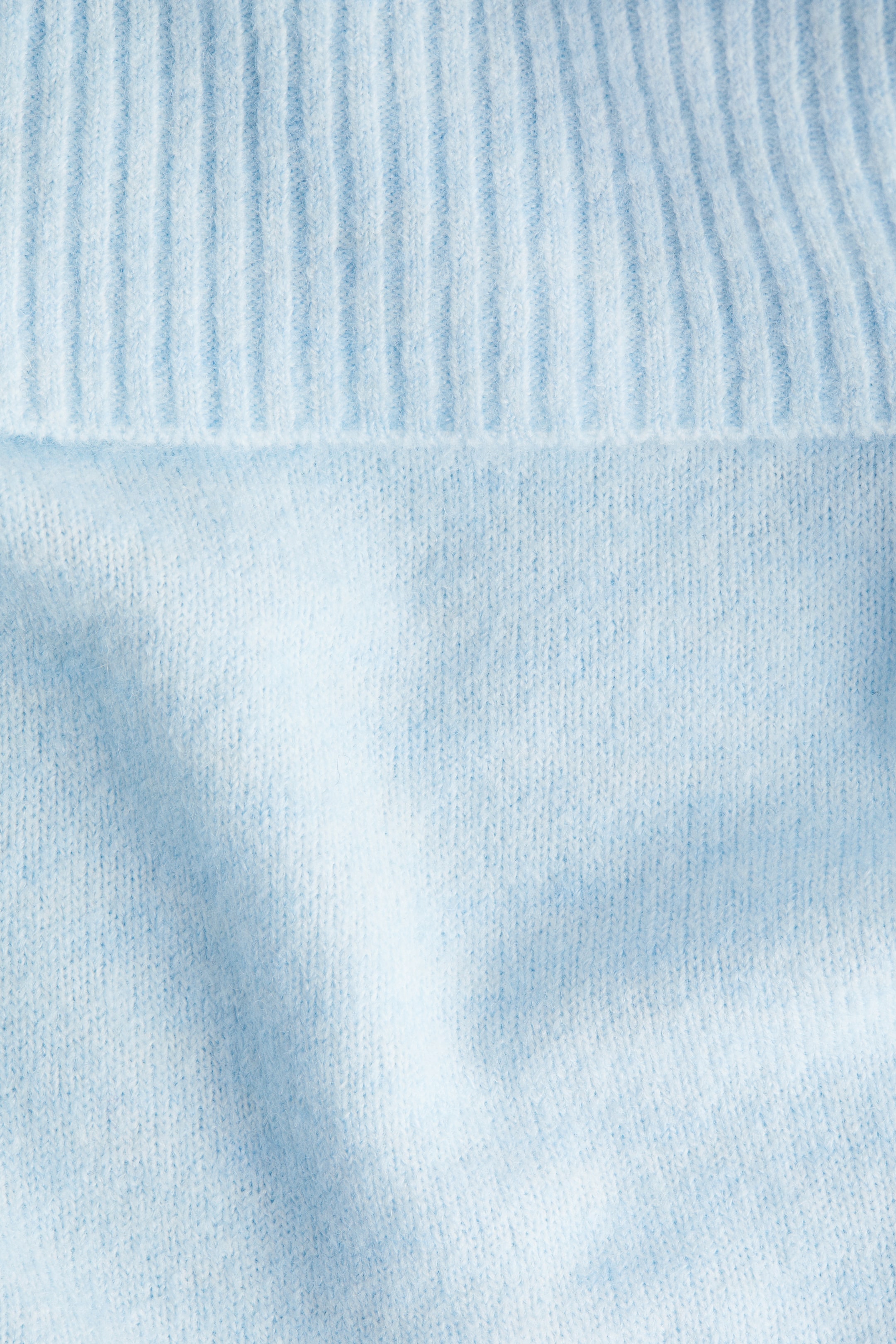 View larger image: A light blue jumper is being presented, highlighting its soft knit construction. A wide, ribbed foldover is being featured at the top of the garment.