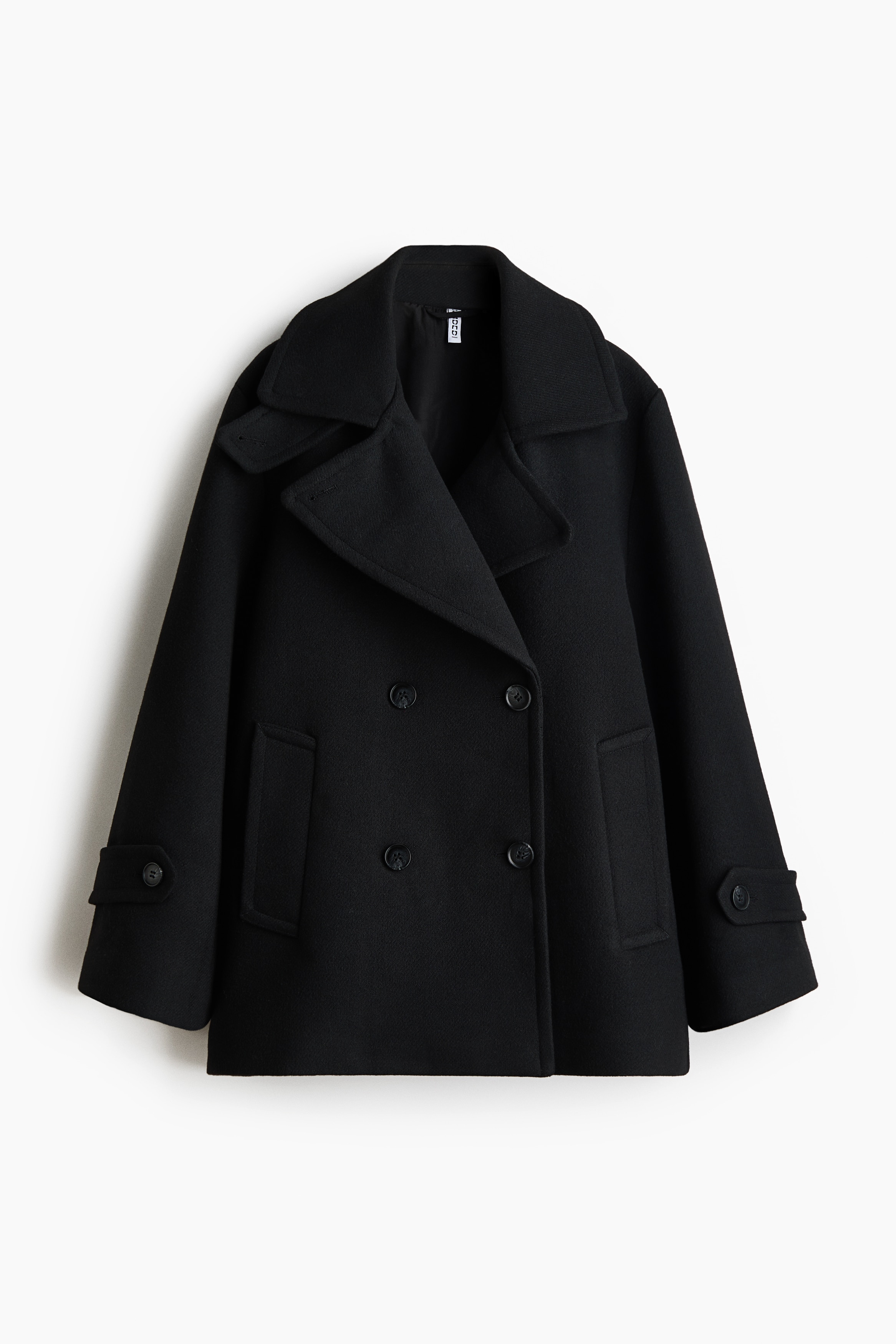 A black double-breasted pea coat in a felted wool blend is shown from the front, styled open over a layered grey hoodie. The coat features prominent notch lapels, double-breasted button detailing, and a relaxed silhouette.