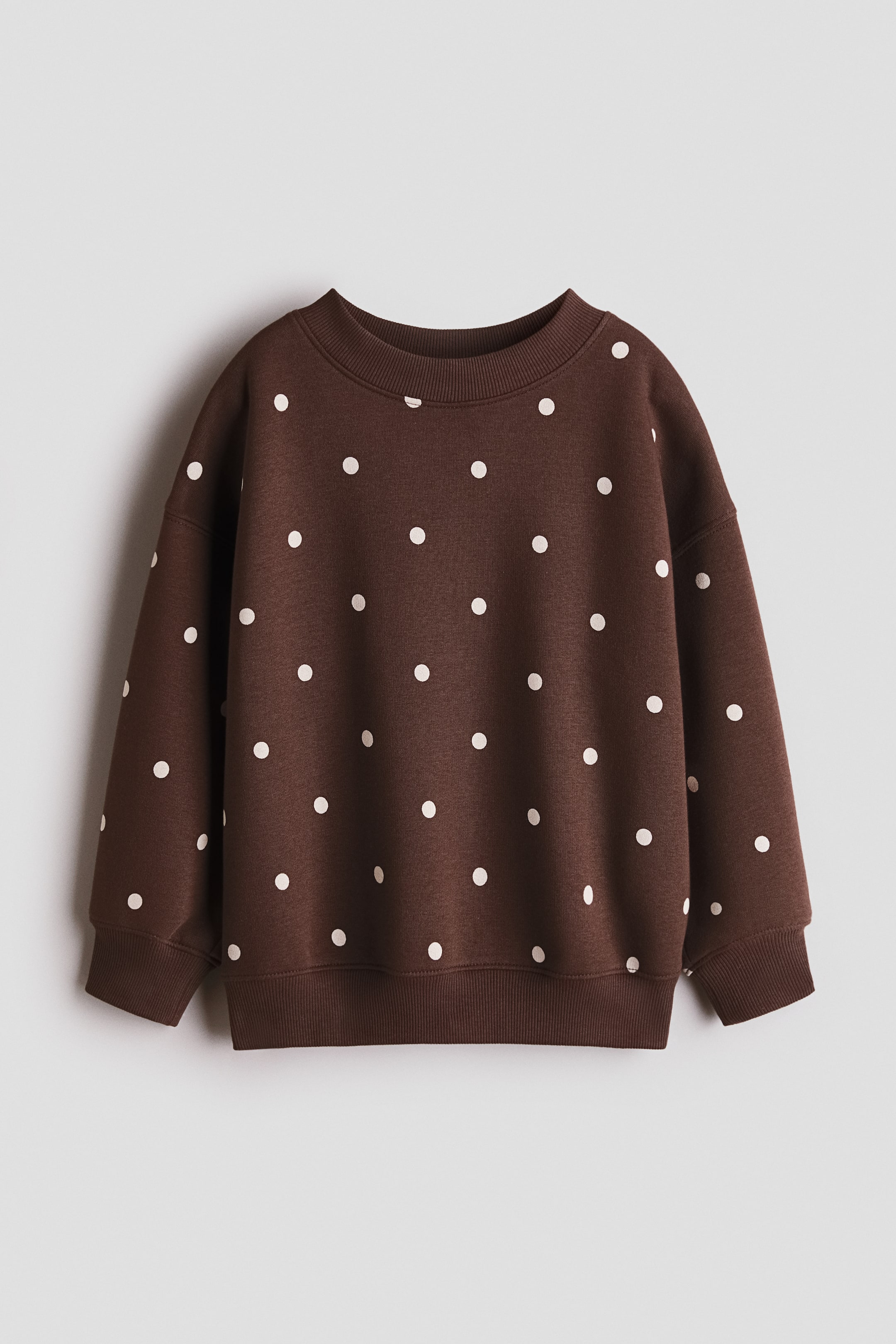 Größeres Bild anzeigen: Ein brauner Sweatshirt zeigt über die gesamte Oberfläche weiße Polka-Dots. Es verfügt über einen gerippten Rundhalsausschnitt, gerippte Bündchen an den langen Ärmeln und einen gerippten Saum, alles flach von vorne präsentiert.