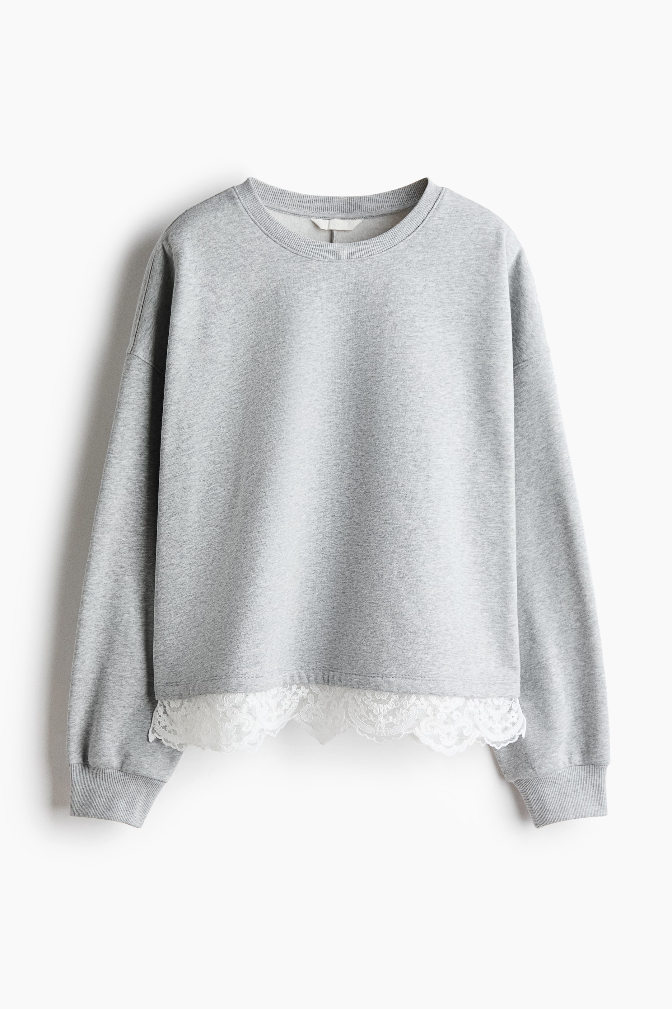 View larger image: A light grey melange sweatshirt is shown from the front, featuring a ribbed crew neck, dropped shoulders, and ribbed cuffs. A wide band of white floral lace trim extends below the hemline, creating a layered effect.