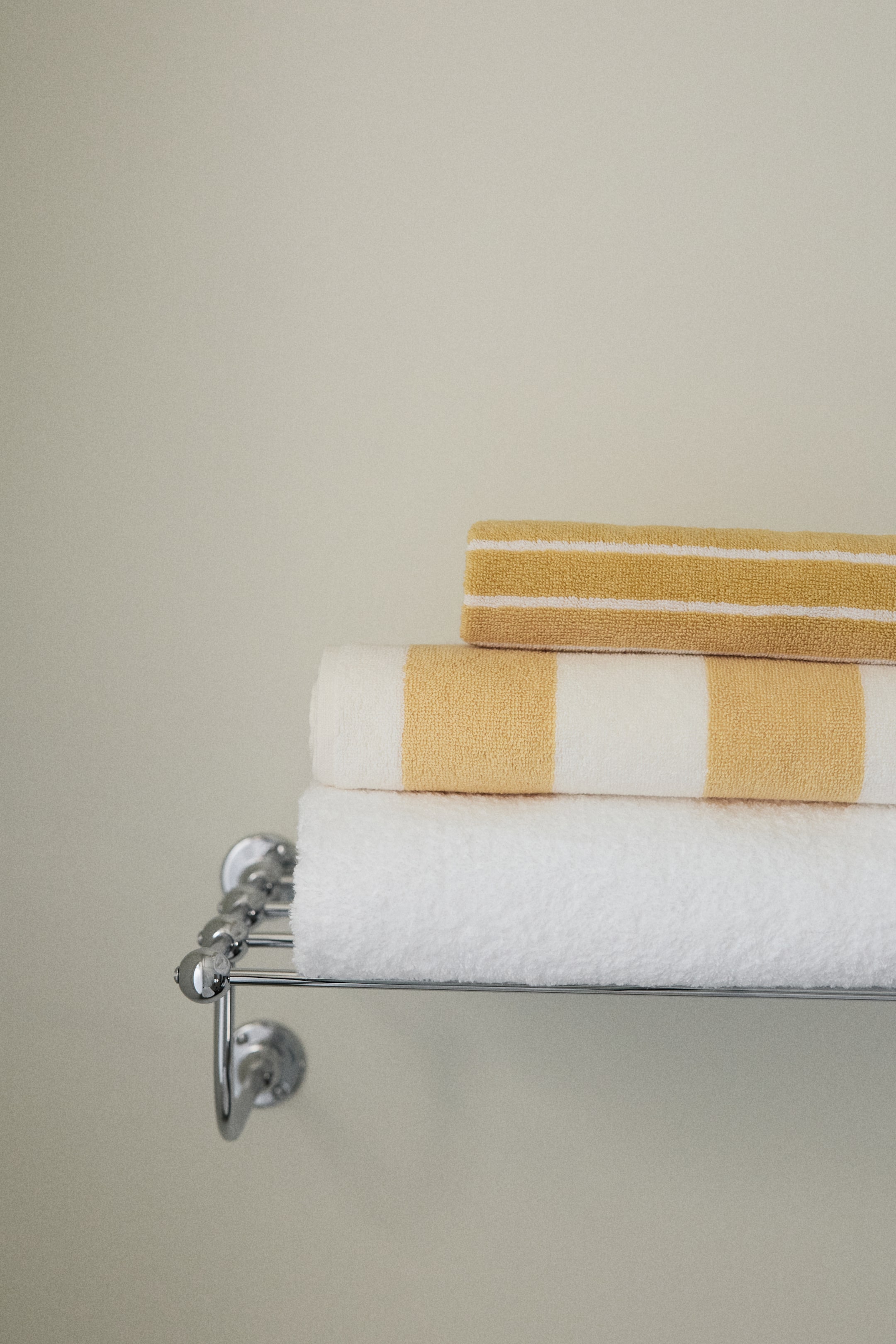 Größeres Bild ansehen: Drei Baumwoll-Frotteehandtücher sind gestapelt und zeigen eine weiche Textur sowie verschiedene Designs. Die oberen beiden Handtücher haben gelbe und weiße Streifen, wobei eines dünne horizontale Streifen und das andere dicke vertikale Streifen aufweist, während ein einfarbiges weißes Handtuch unten liegt.