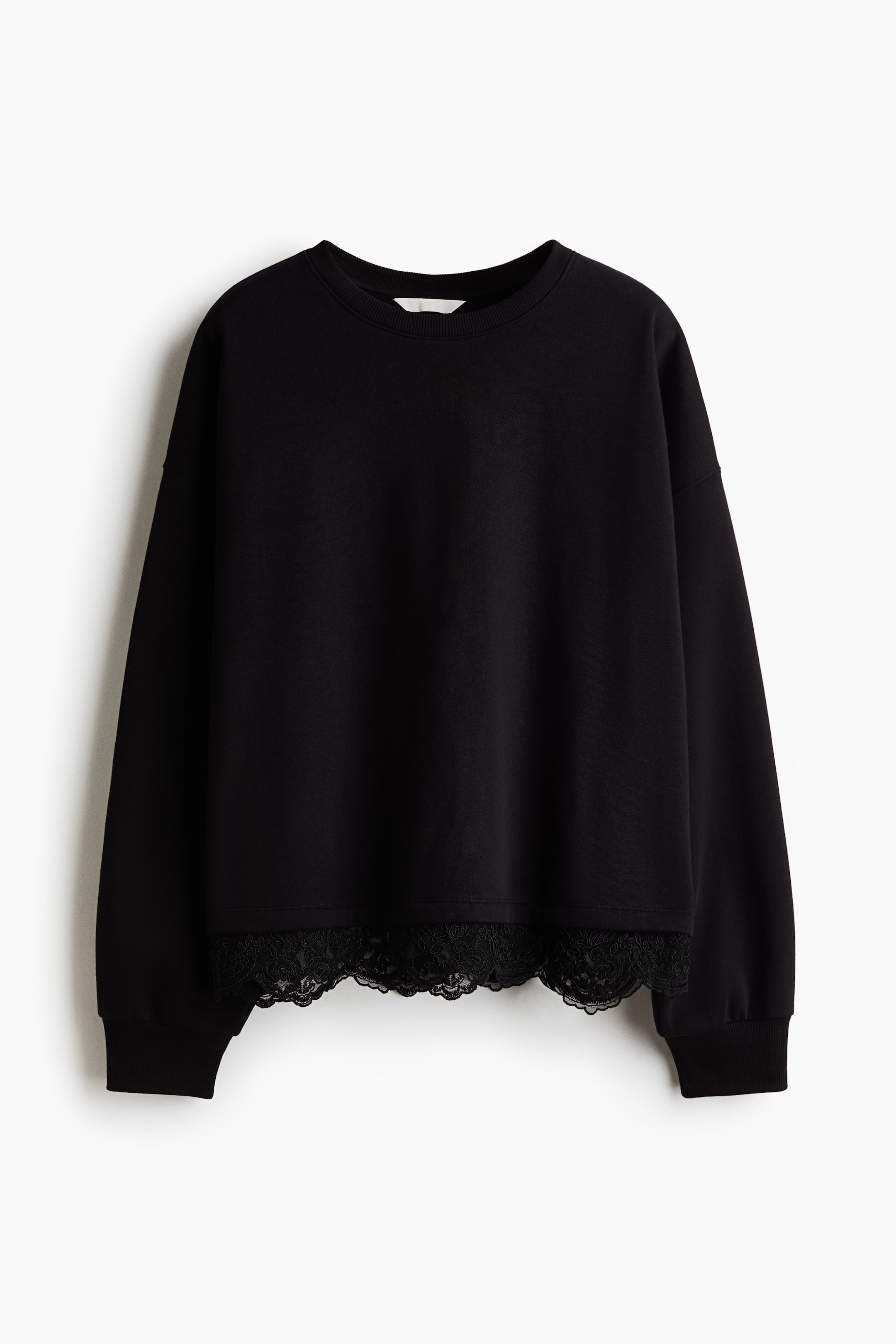 View larger image: A black crewneck sweatshirt is shown from the front, featuring dropped shoulders, long sleeves with ribbed cuffs, and a relaxed silhouette. The bottom hem is finished with a delicate black scalloped lace trim.