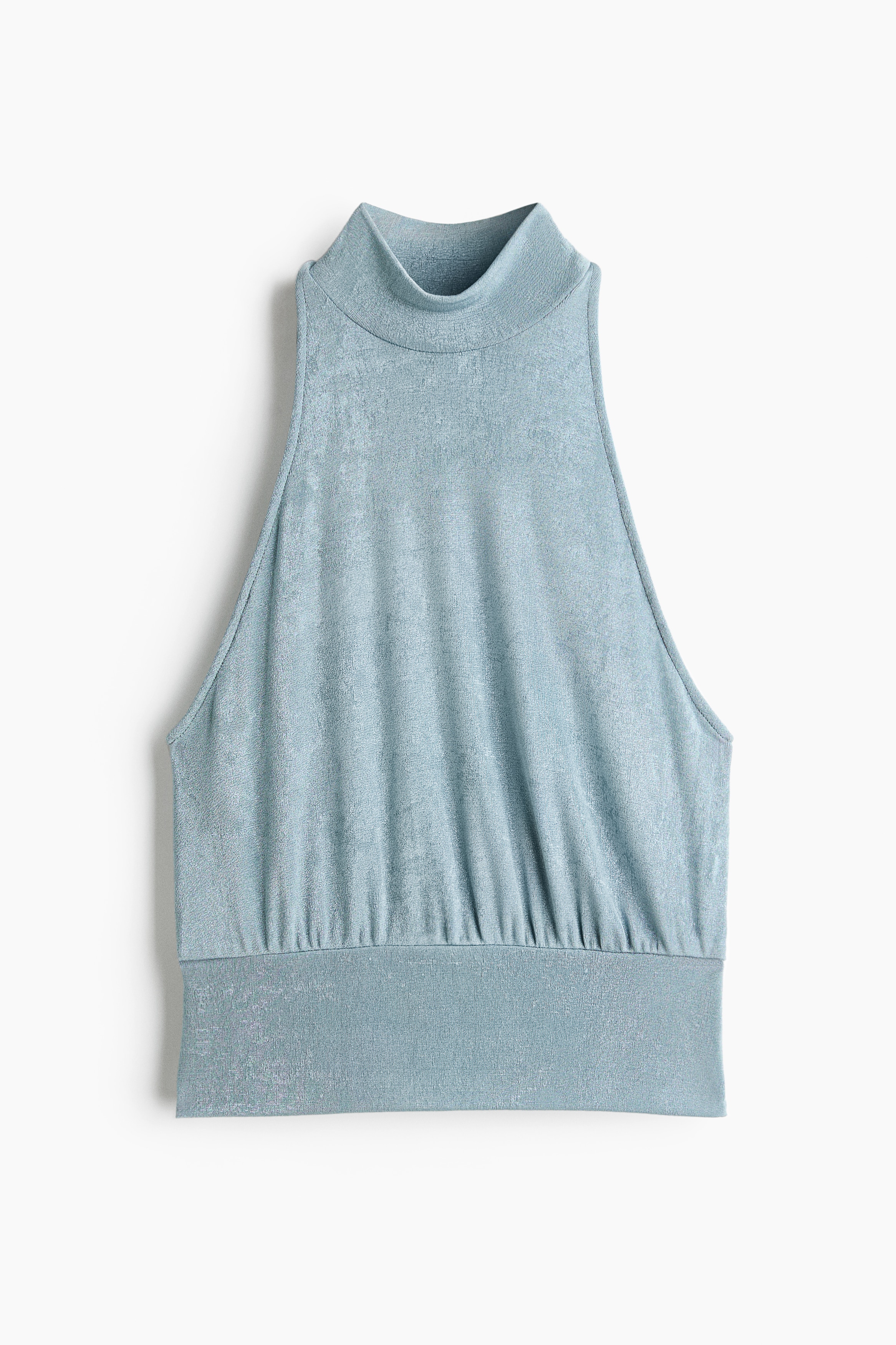 La modelo lleva una blusa de jersey azul claro, sin mangas, con cuello alto y recto, y un corte estrecho en los hombros. La blusa estÃ¡ estilizada por dentro de un pantalÃ³n blanco.
