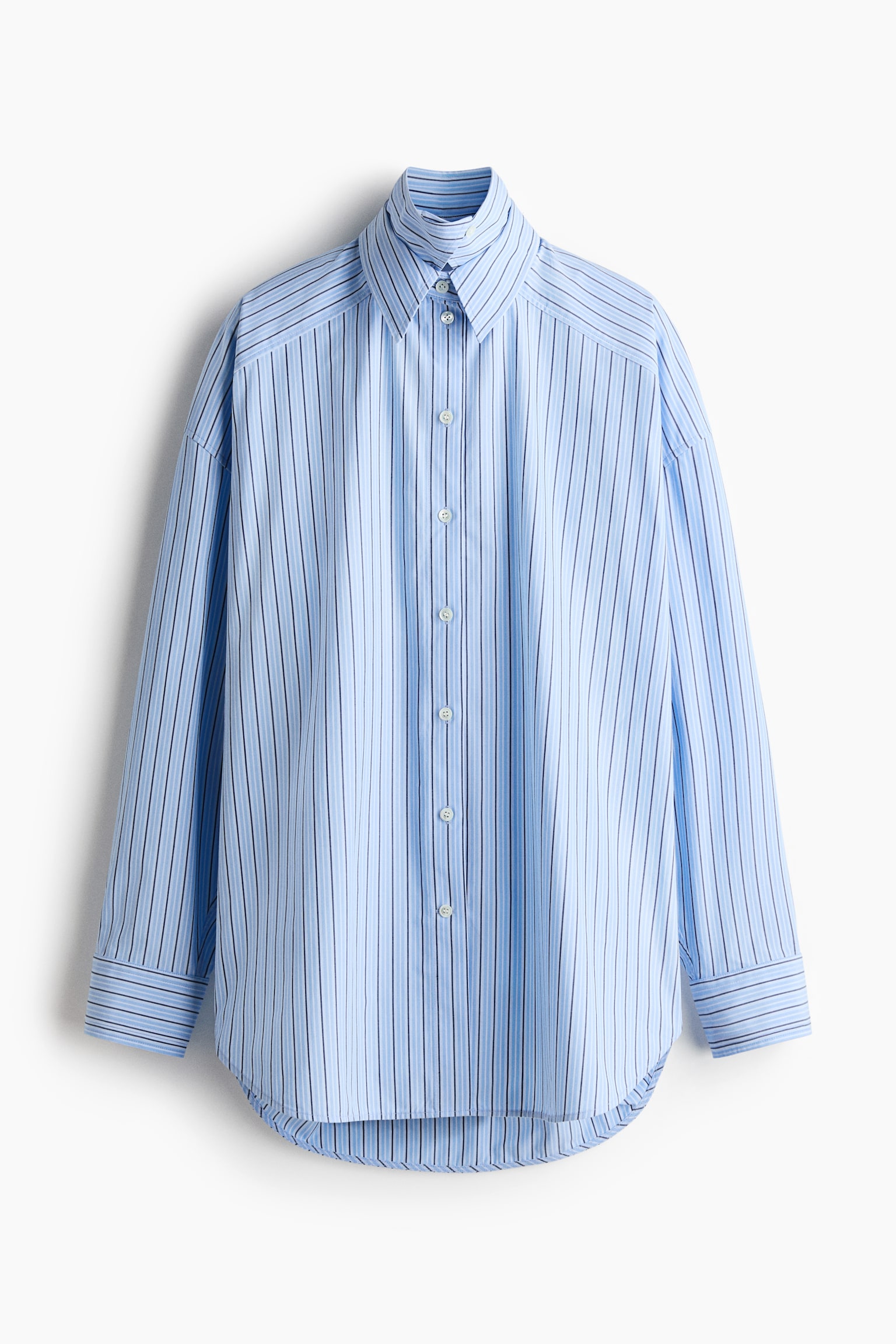 A light blue long-sleeved button-up shirt is showcasing its front, featuring vertical stripes of alternating light blue and dark blue. It is crafted with a pointed collar, a full button placket with white buttons, buttoned cuffs, and a curved hem, offering an oversized fit. - 1