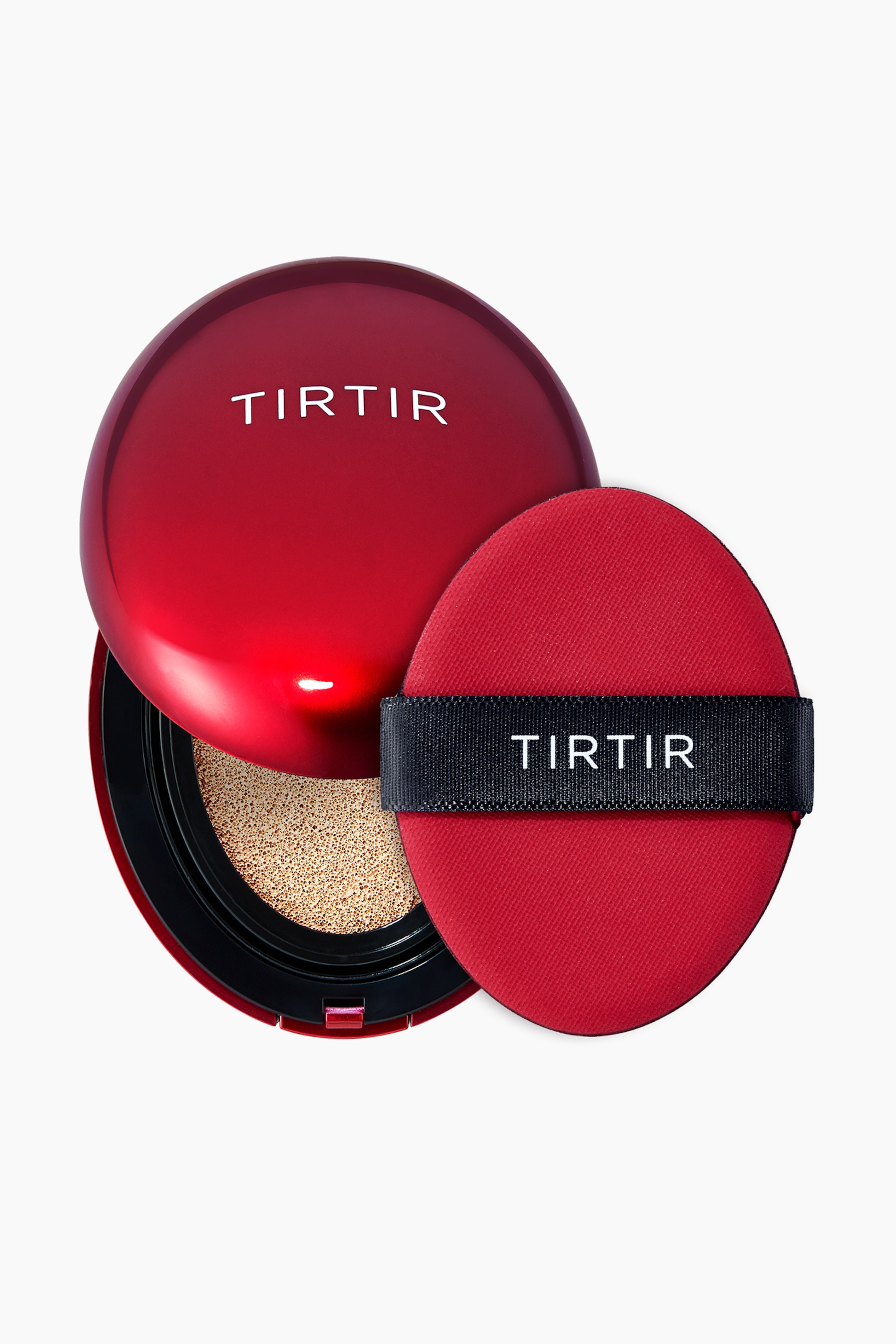 Vis større bilde: En rød, blank, rund TIRTIR cushion foundation-kompakt vises med lokket delvis åpent, og avslører en beige porøs pute inni. En matchende rød ovalformet puff, med et svart båndhåndtak med "TIRTIR" trykt i hvitt, hviler ved siden av kompaktet.