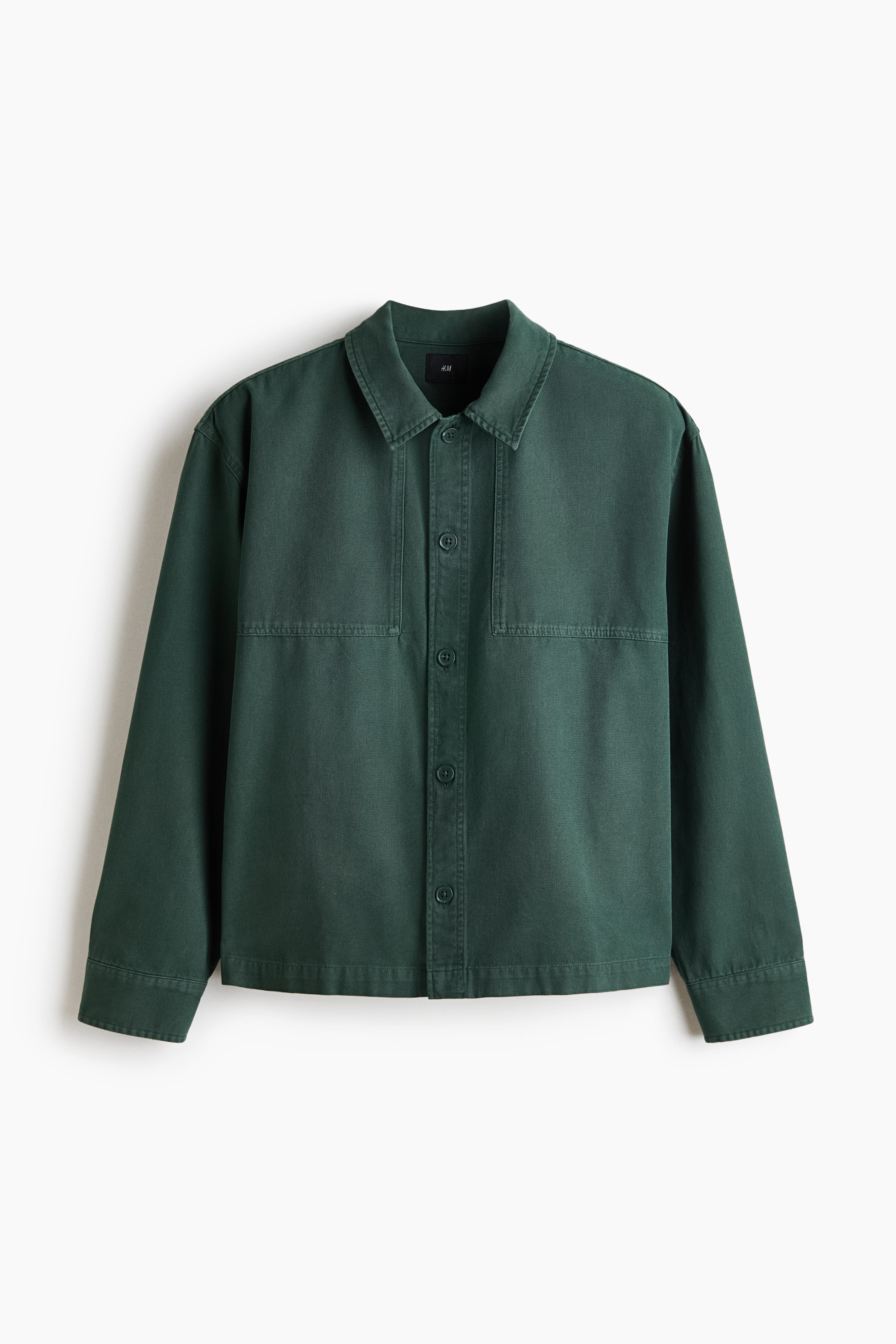 View larger image: A dark green utility overshirt is facing straight on, featuring a pointed collar and a button-front placket with dark buttons. It is displaying two flap chest pockets with visible topstitching and long sleeves with simple, straight cuffs.