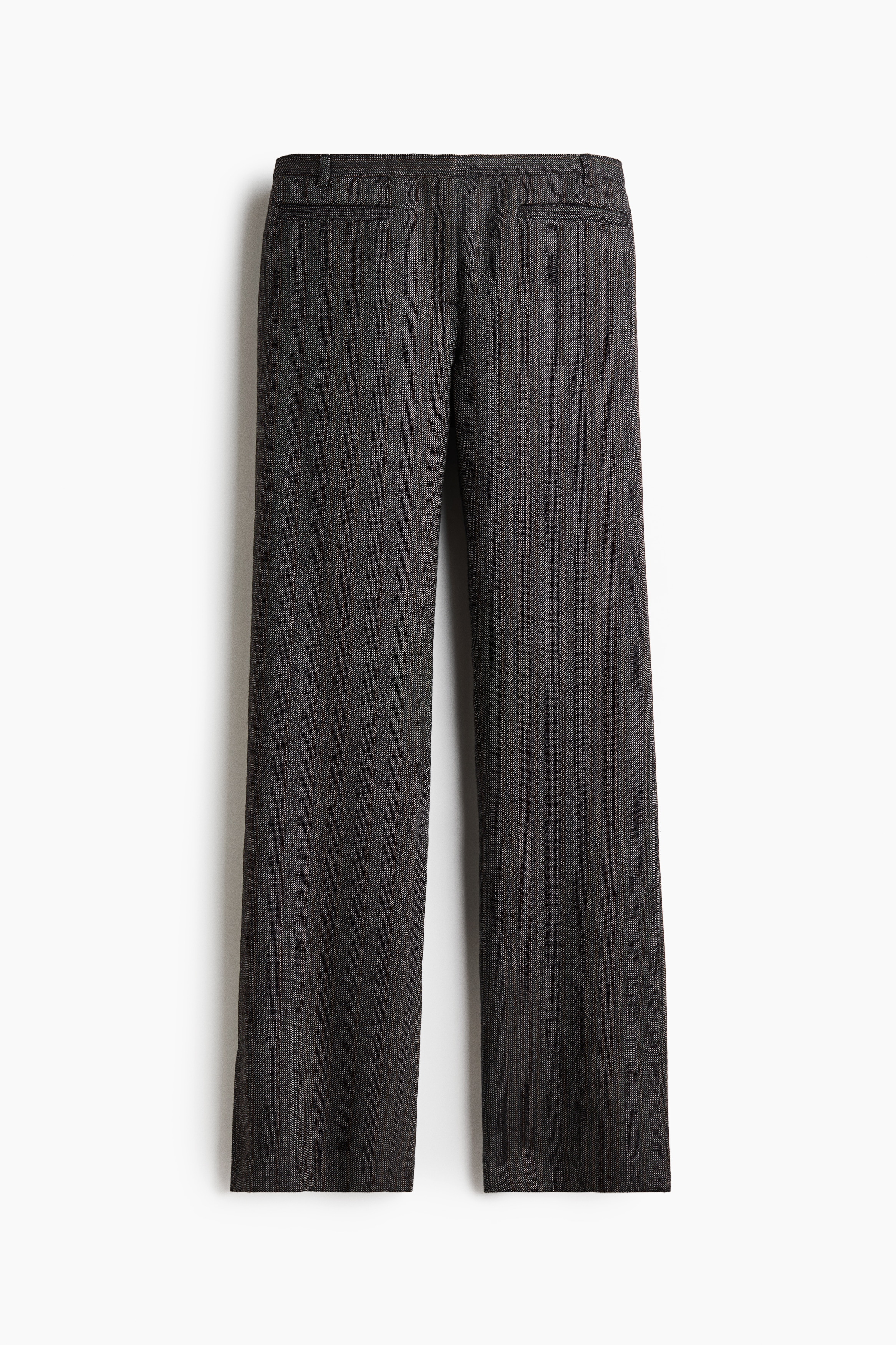 Le mannequin porte un pantalon en laine tissée texturée grise, avec une taille basse, des jambes droites et de hautes fentes à lâourlet. Le pantalon est associé à un blazer gris assorti, drapé sur les épaules, ainsi quâà un top vert foncé à col montant.