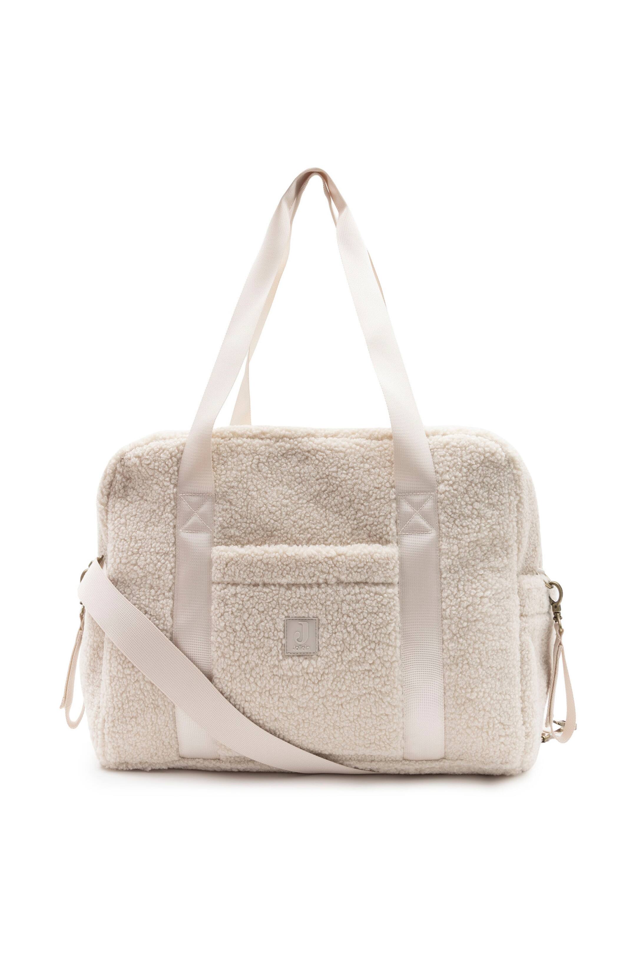 Agrandir l'image: Un sac à langer en polaire teddy couleur crème est présenté debout, de face, mettant en valeur un extérieur doux et texturé avec une poche plaquée à l'avant et un petit patch logo carré. Il affiche deux anses tissées sur le dessus, des poches latérales et une bandoulière réglable drapée sur l'avant.