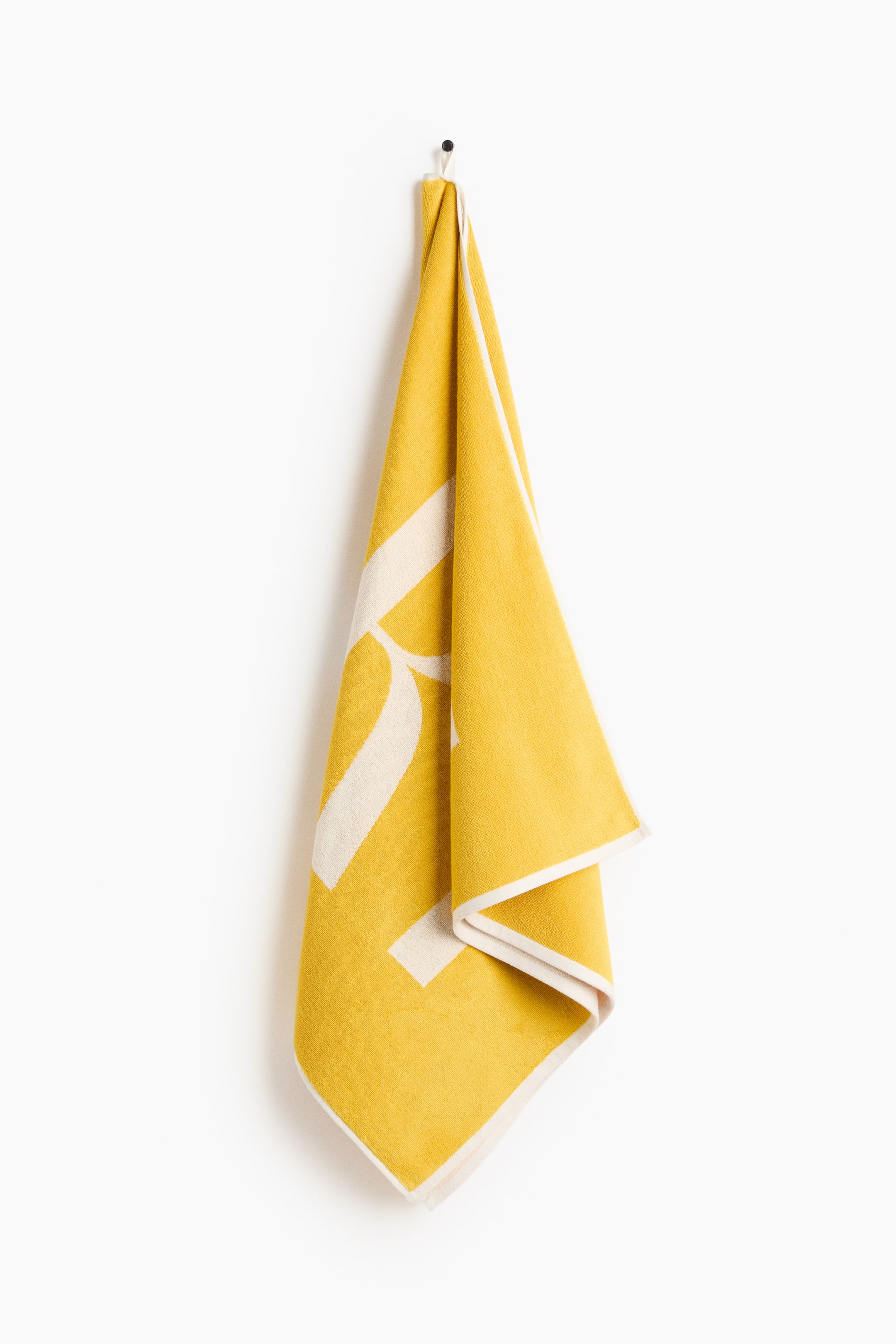 View larger image: A yellow towel, adorned with large, off-white graphic elements and an off-white border, is neatly folded and hanging from a hook.