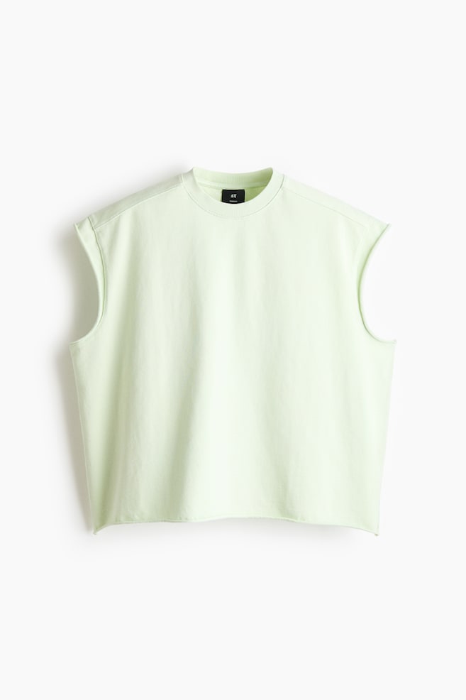 Ein hellgrünes, ärmelloses Sweatshirt wird von vorne präsentiert, mit einem gerippten Rundhalsausschnitt und überschnittenen Schulternähten. Die Armlöcher und der abgeschnittene Saum am unteren Rand zeigen rohe, geschnittene Kanten. - 1