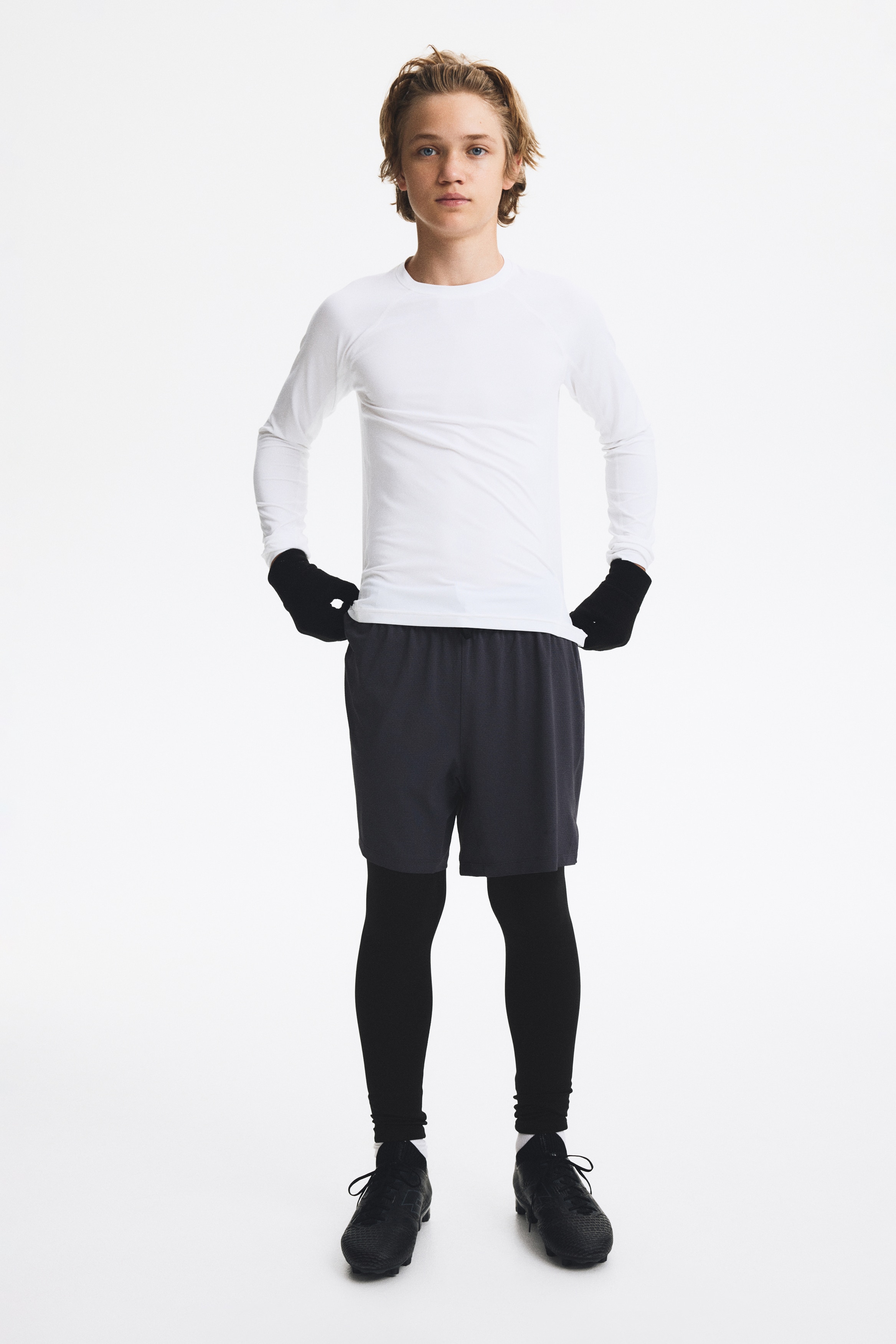 Een paar twee-in-Ã©Ã©n sportbroeken met grijze, getextureerde shorts over geÃ¯ntegreerde zwarte leggings, weergegeven van voren. De buitenste shorts hebben een elastische tailleband met een zwart trekkoord en zijsplitten aan de zoom.