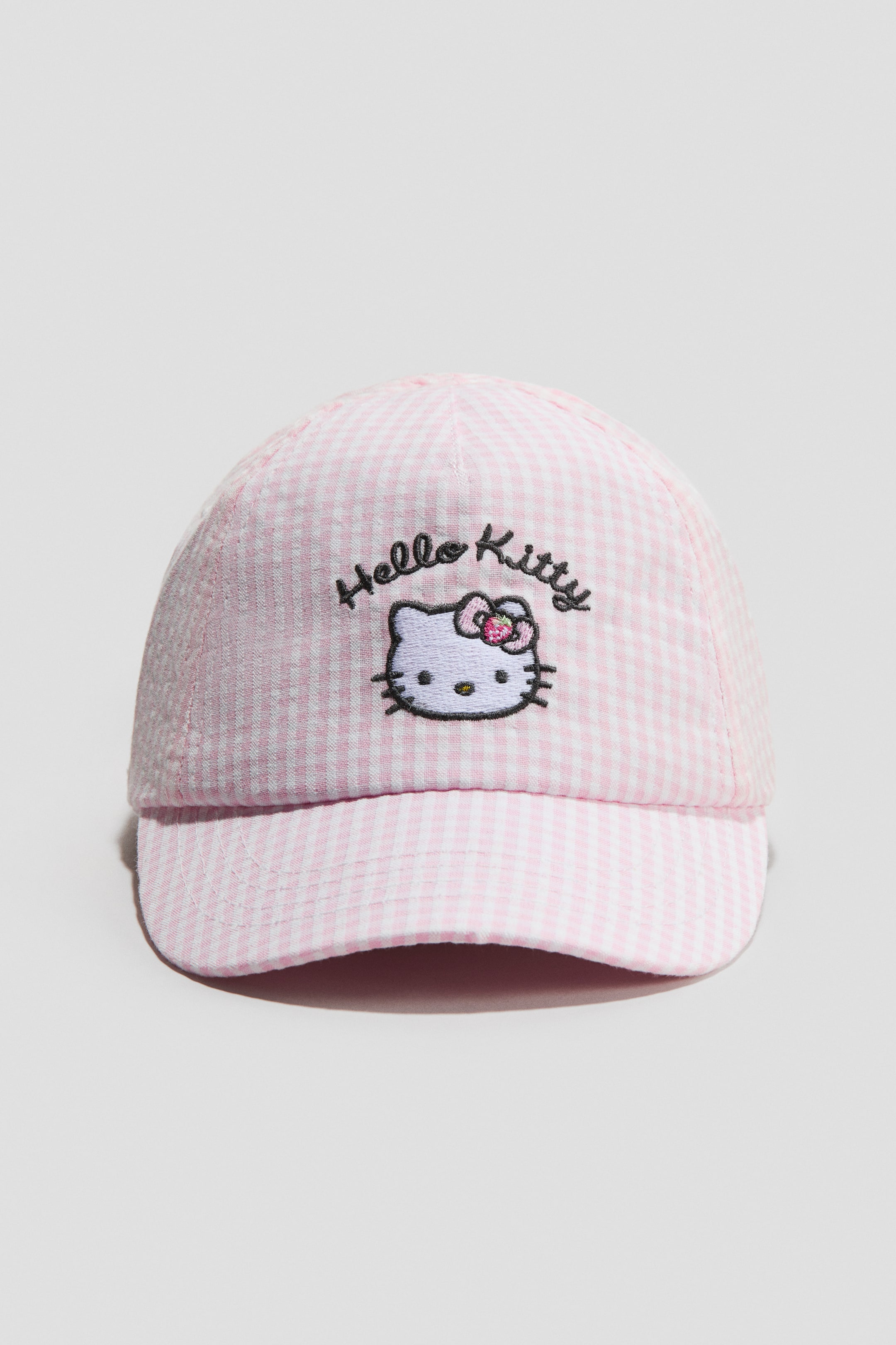 Ampliar la imagen: Una gorra, con la parte delantera hacia el FRENTE, muestra un patrón de cuadros vichy rosado y blanco. Un motivo bordado de Hello Kitty, con el personaje y texto, es visible en su panel frontal.