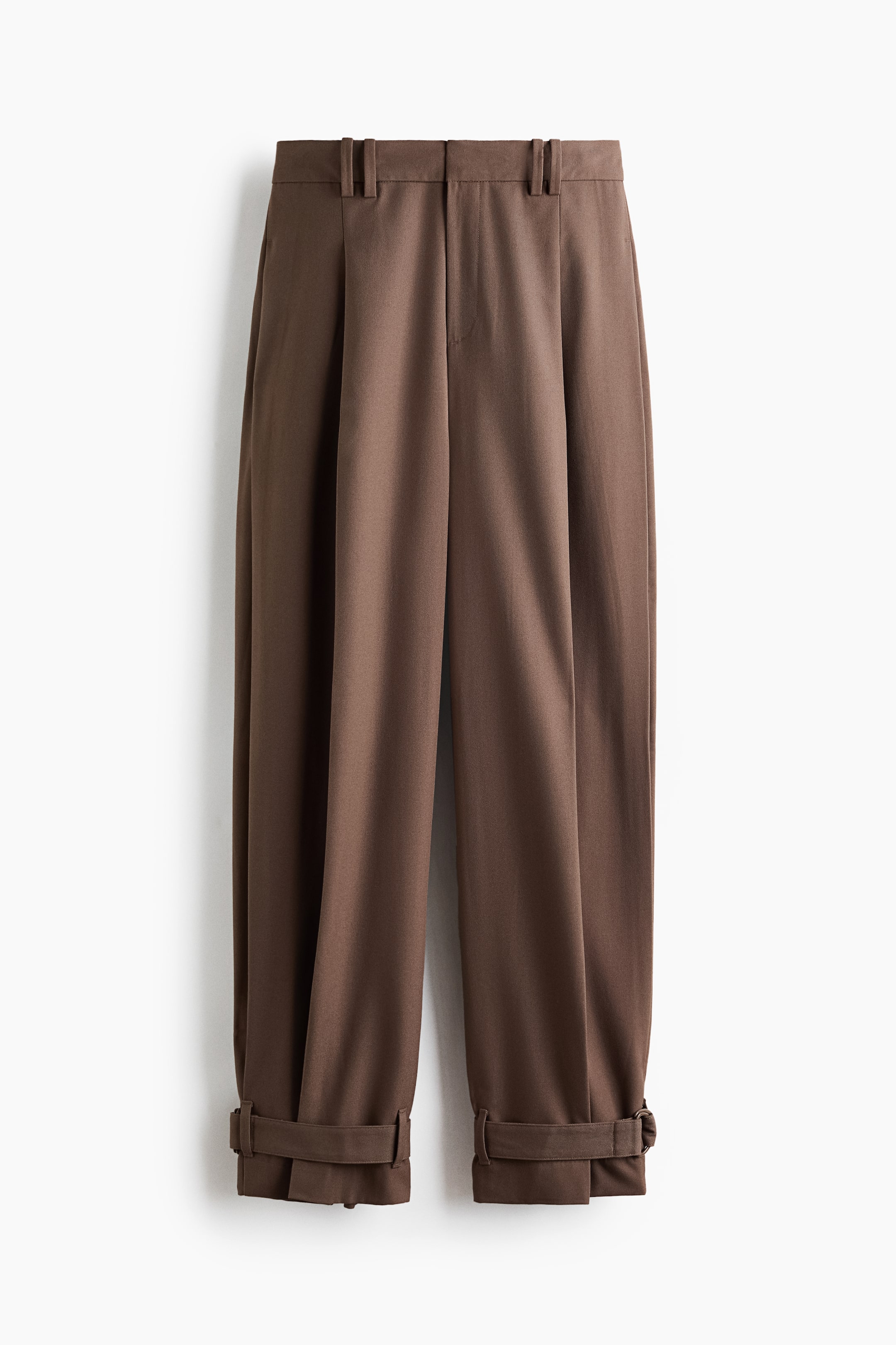 View larger image: Brown wide-leg trousers are showcasing a front perspective, highlighting single pleats at the waist and adjustable cuffs with tabs at the ankles.