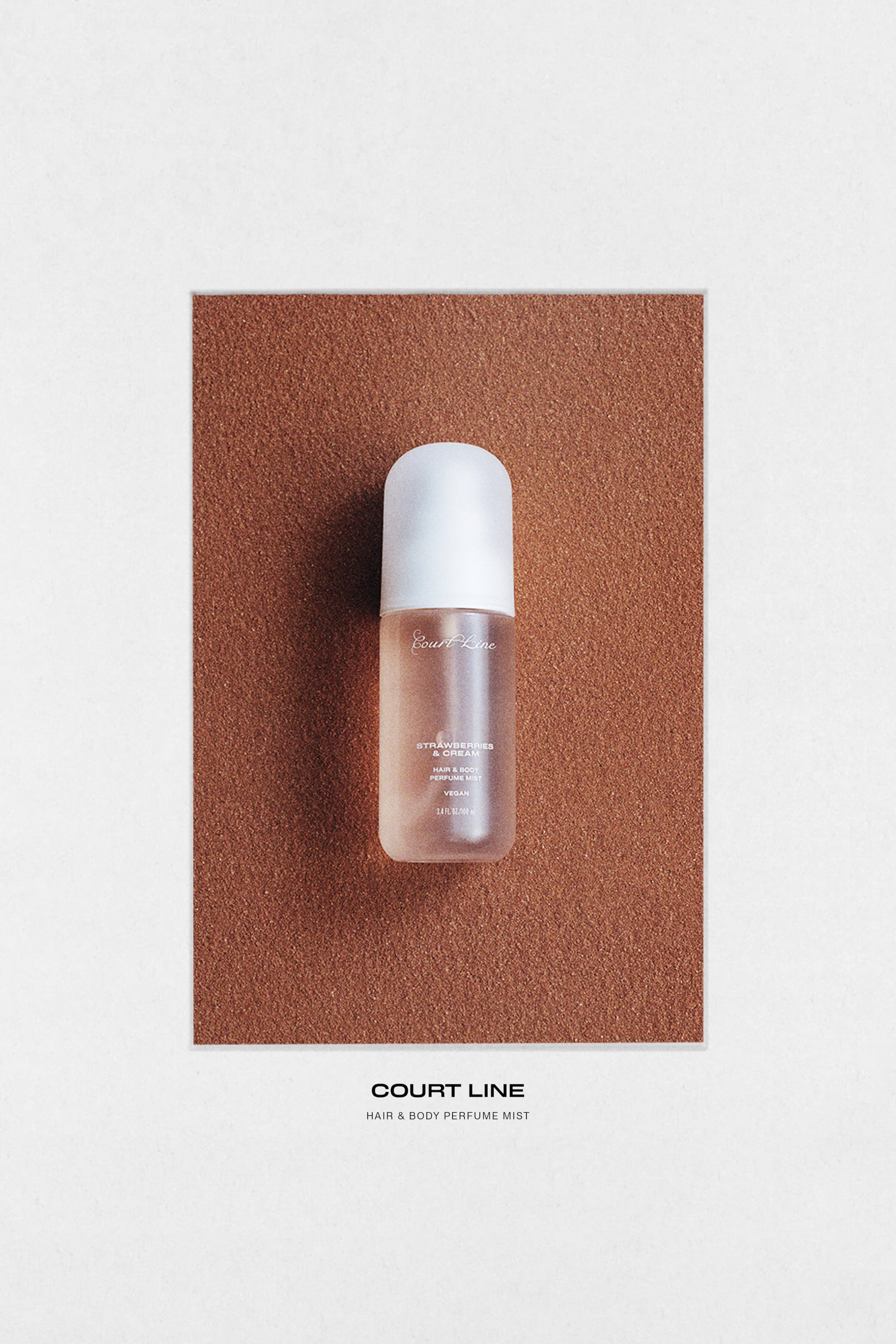View larger image: A frosted glass hair and body mist bottle is standing upright, containing a light pink liquid and topped with a white, opaque, rounded cap. The bottle's front label displays 'Court Line', 'Strawberries & Cream', 'Hair & Body Perfume Mist', 'Vegan', and '3.4 fl. oz / 100 ml'.
