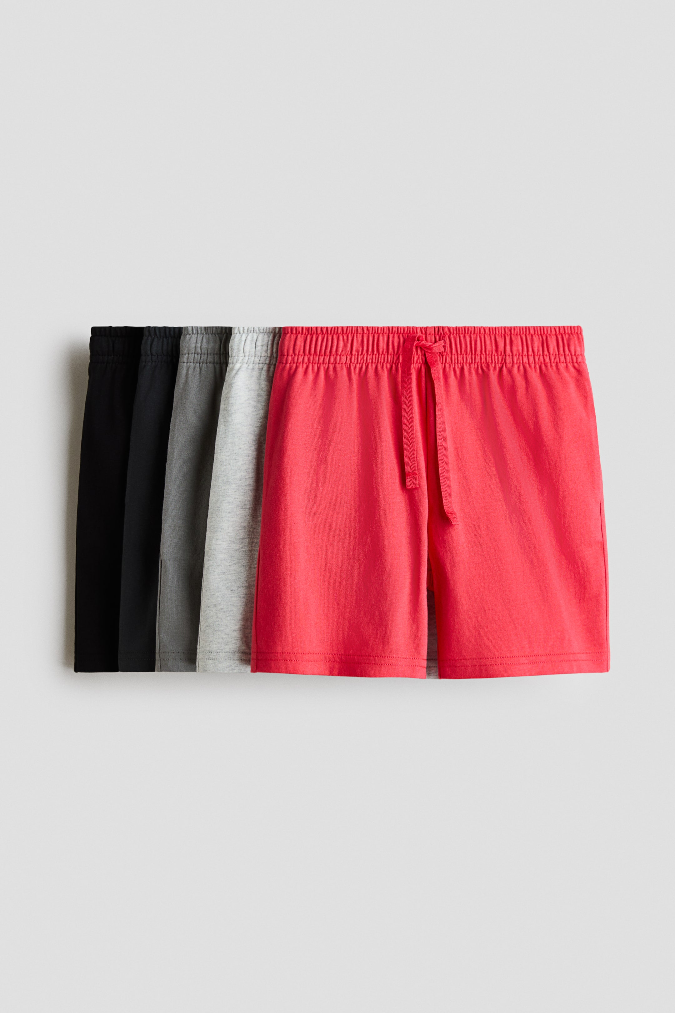 Voir une image plus grande: Cinq paires de shorts en jersey de coton doux sont disposées en éventail superposé, avec la paire rouge à l'avant affichant clairement une taille élastique avec cordon de serrage. Les shorts présentent des ourlets simples et sont disponibles en noir, gris foncé, gris moyen, gris clair et rouge.