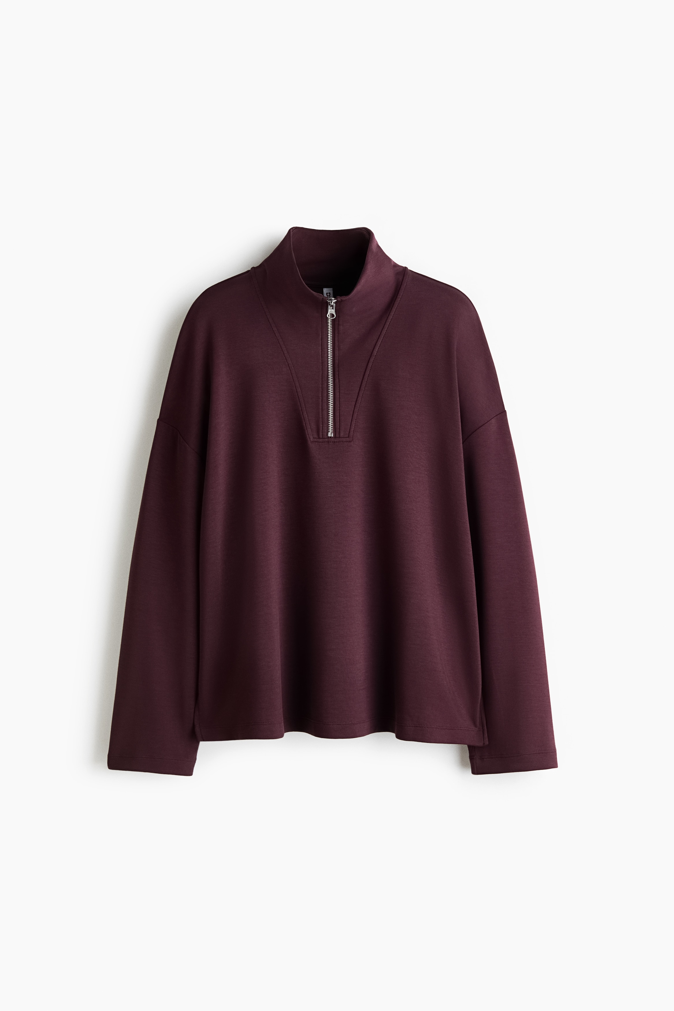 A burgundy half-zip sweatshirt featuring a high collar and a silver metal zip is being worn by the model. The loose-fitting, long-sleeved pullover is paired with matching burgundy trousers.