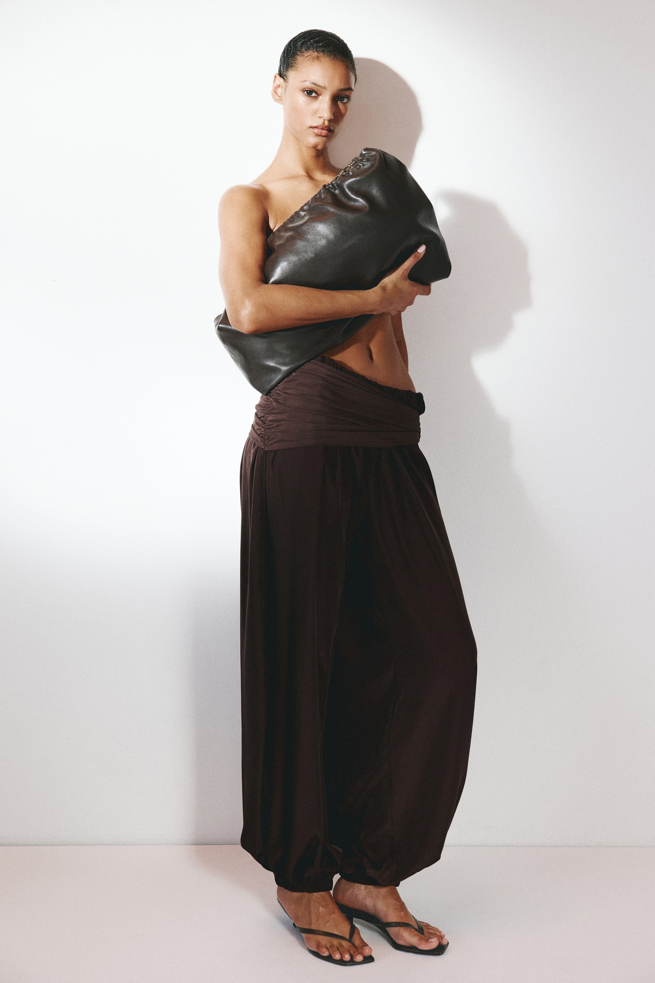 View larger image: "A dark brown, oversized, slouchy clutch bag is being held close to the body, showcasing its gathered opening and soft, pliable structure."