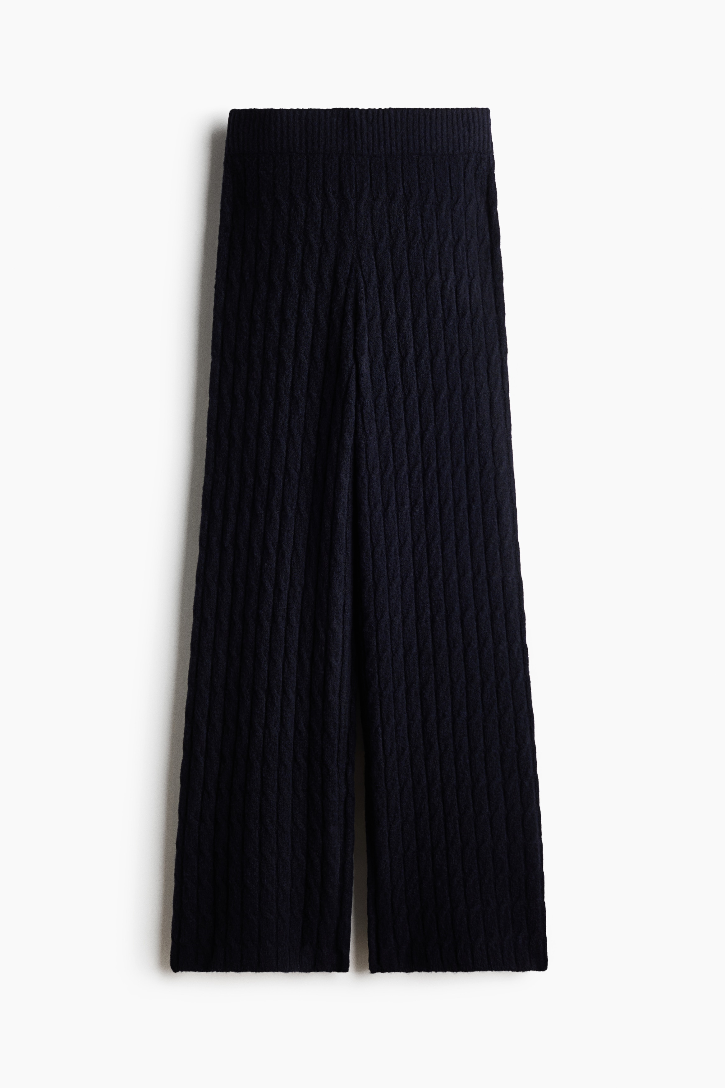 Sorte kabelstrikkede bukser med ribbet talje og afslappede, lige ben bÃ¦res af modellen. Bukserne er stylet med en matchende sort kabelstrikket sweater, lagt over en hvid langÃ¦rmet top.