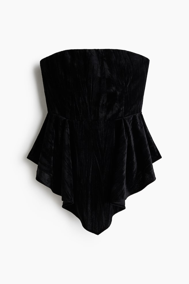 A black strapless top is shown from the front, featuring a fitted bodice made of textured, crushed velvet and flaring into a draped peplum waist with an asymmetrical, pointed handkerchief hemline. - 1