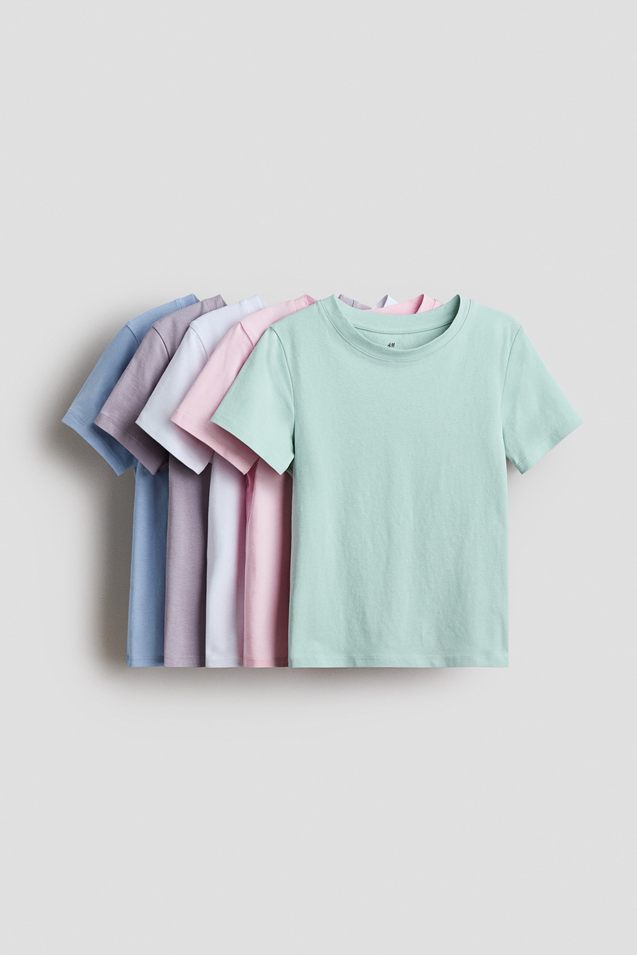 View larger image: "T-shirts made from soft cotton jersey are perfect for layering and come in a variety of pastel colors. The mint green t-shirt is prominently displayed at the front. Each t-shirt features a ribbed neckline and slightly dropped shoulders."
