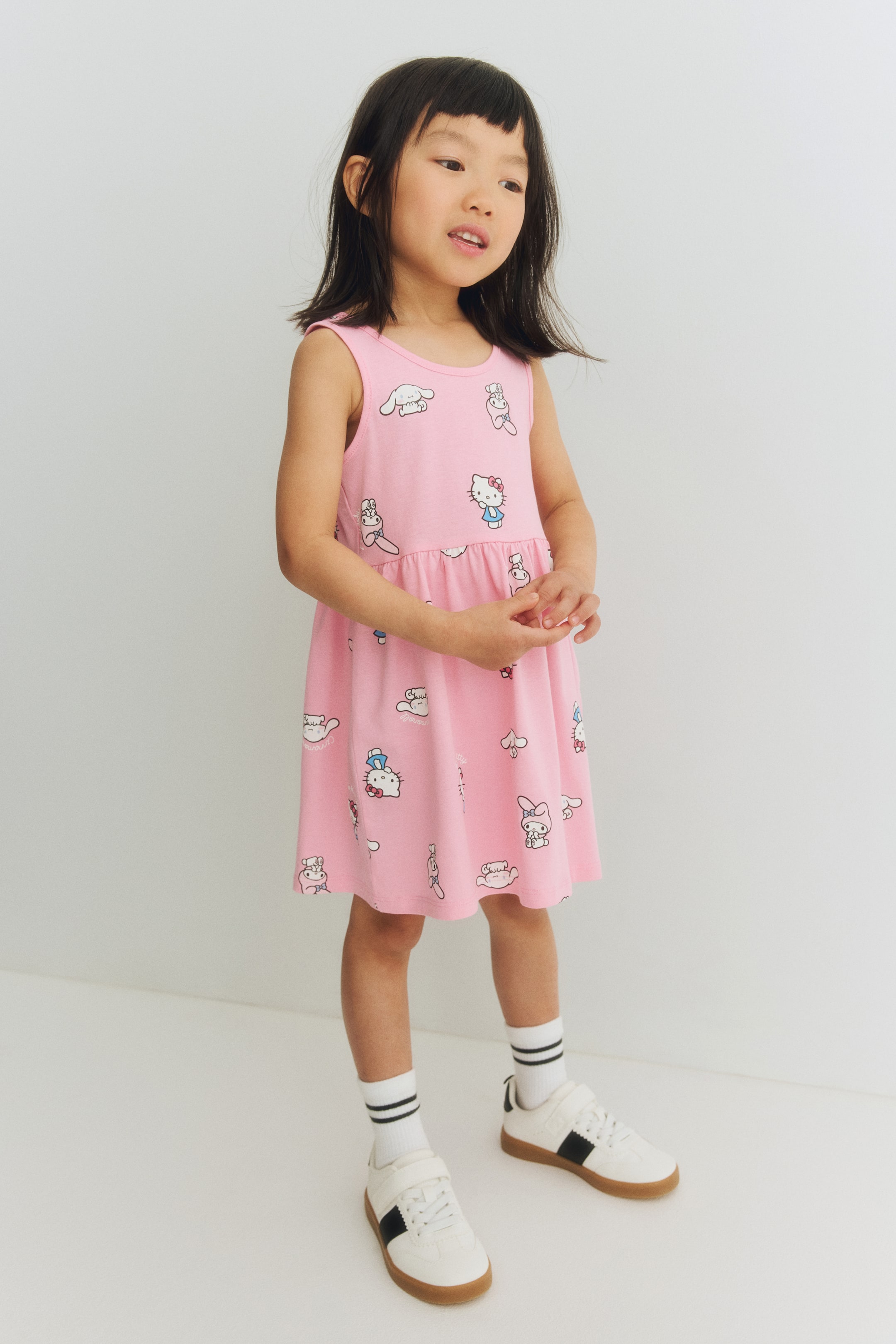 View larger image: A pink sleeveless dress featuring an allover print of various Sanrio characters. Designed with a round neck and a gathered waist, it flows into an A-line skirt that reaches above the knees.
