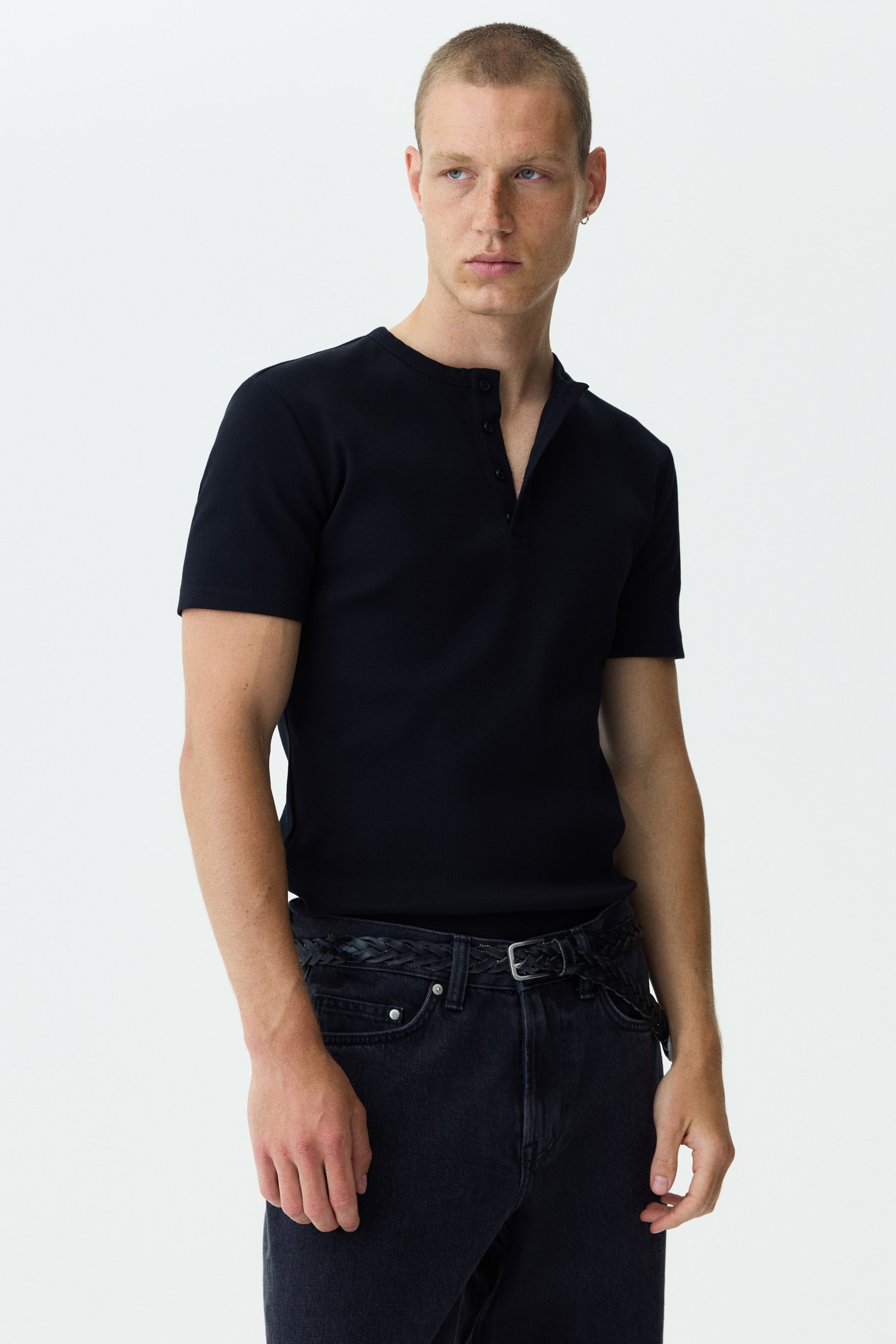 View larger image: A dark blue ribbed short-sleeved Henley shirt, featuring a round neckline and a three-button placket, showcases a slim fit while being worn tucked into dark jeans.