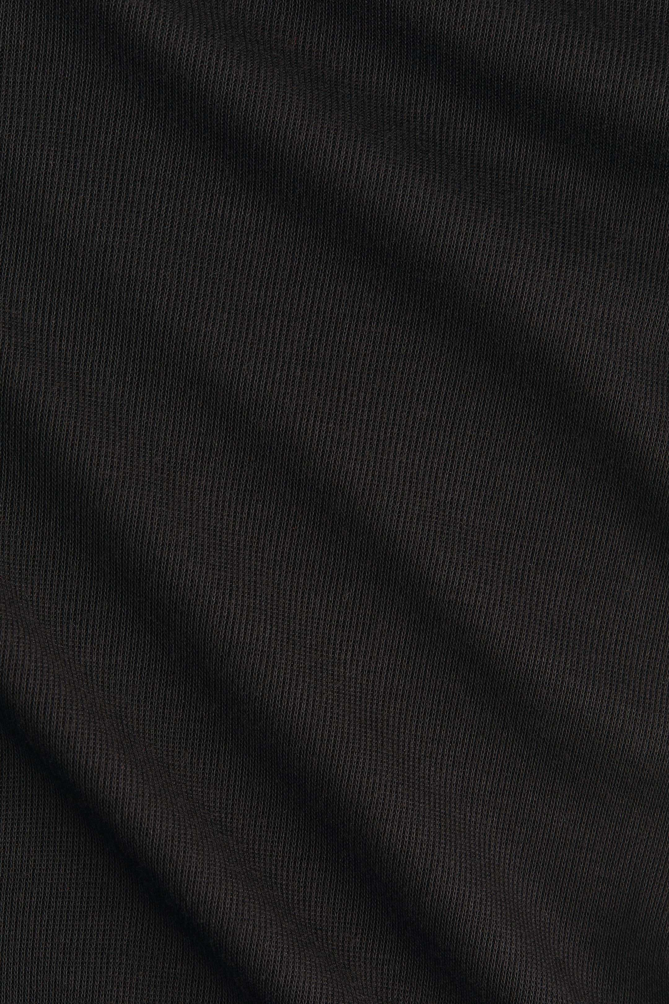 Ampliar la imagen: Una tela de punto fino en color negro está mostrando su sutil textura vertical y pliegues suaves, que crean sombras tenues a lo largo de su superficie.