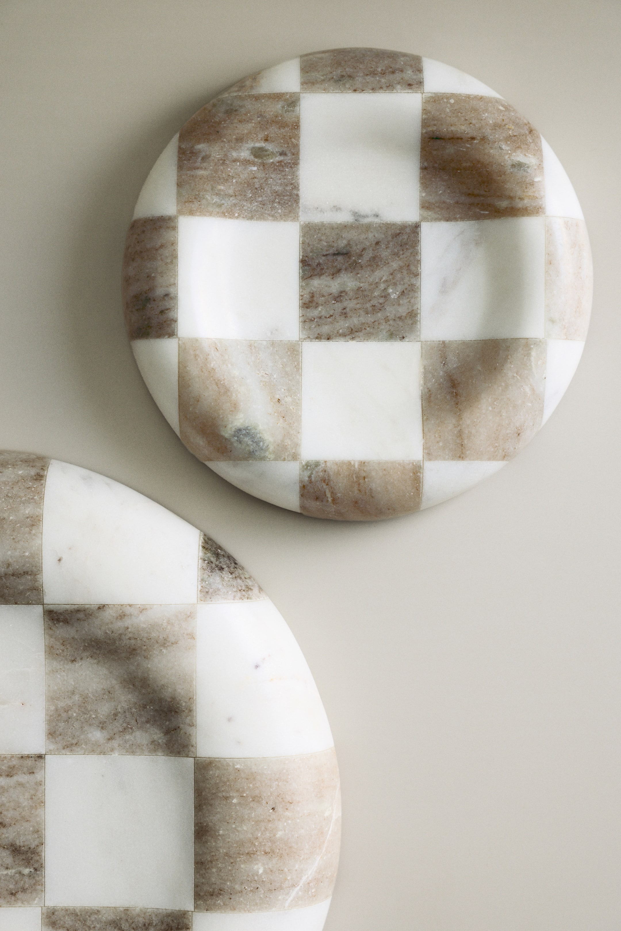 View larger image: A round marble board features a chequered pattern of alternating solid white and naturally veined light-brown squares. It lies flat in a top-down view, with a similar board partially visible beneath it.