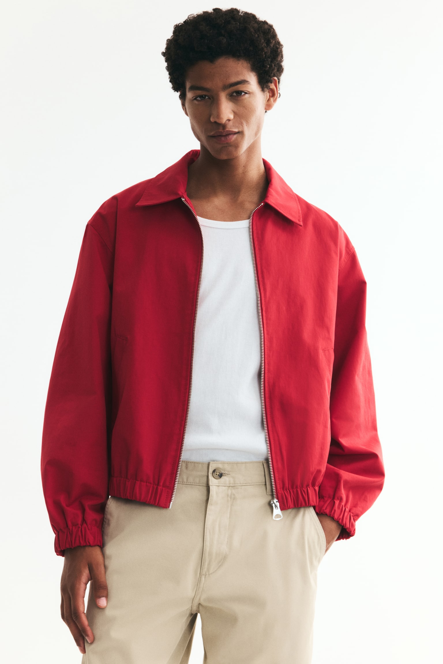A red jacket is facing front, featuring a turn-down collar, a zip running down the front, two front welt pockets, and covered elastication at the cuffs and hem. - 1