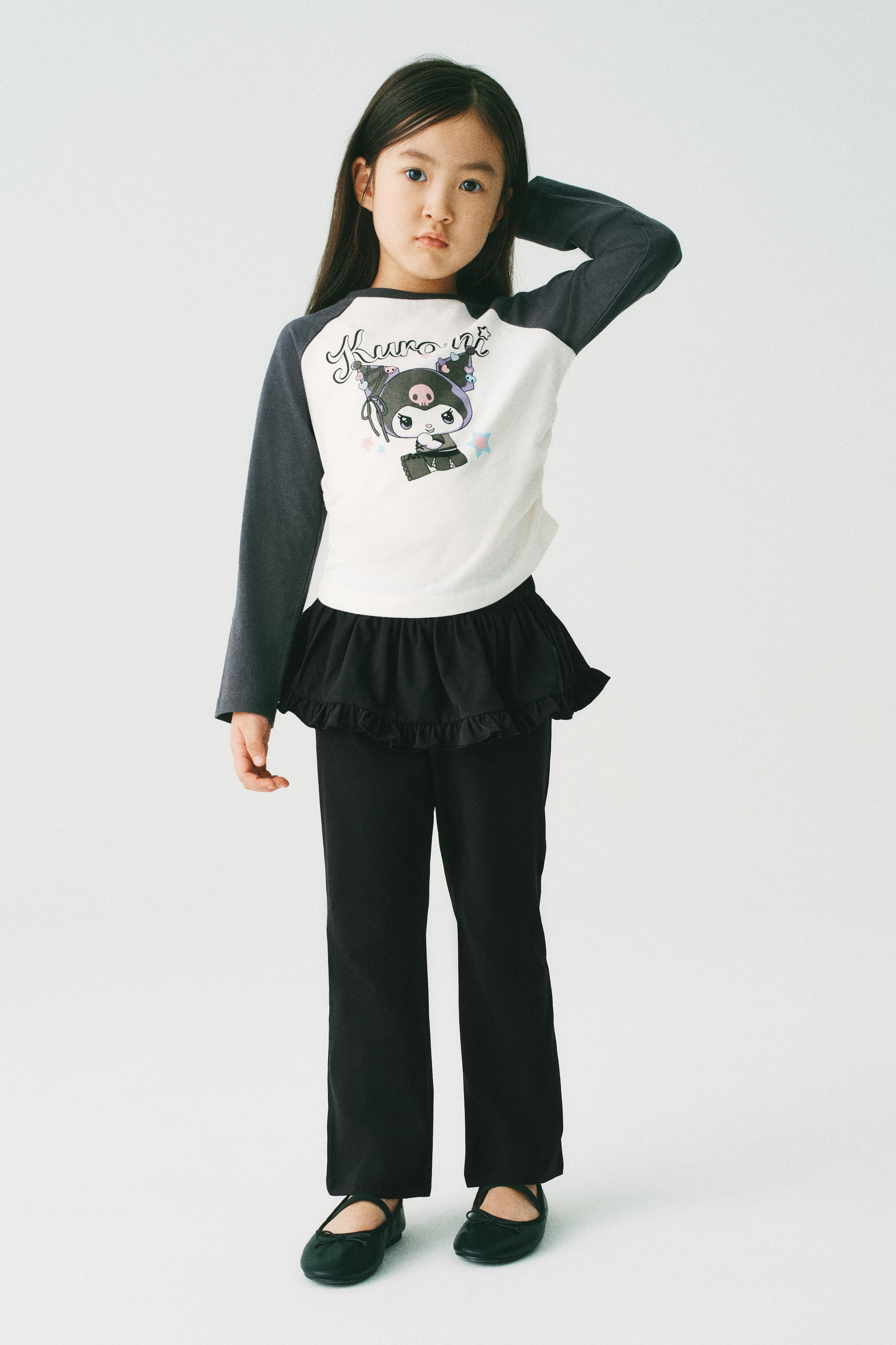 拡大画像を表示: モデルが着用しているのは、ブラックのフレアでゆったりとしたフィット感のあるパンツです。上部にオーバーロックされたフリルトリムが施されたフレアスカートレイヤーが付いています。